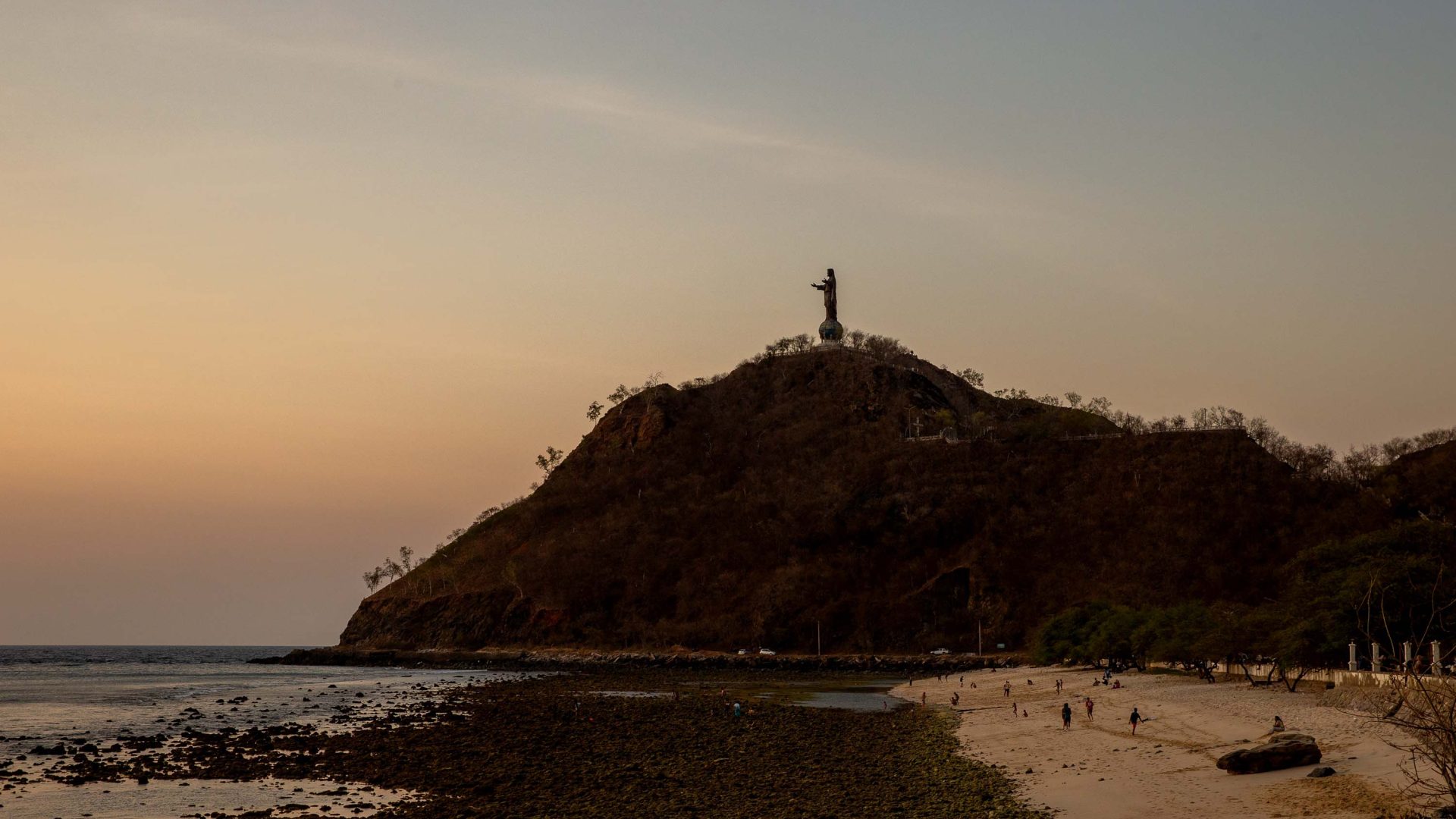 The soft light of dusk over a mountain with a statue of Christ at its summit.