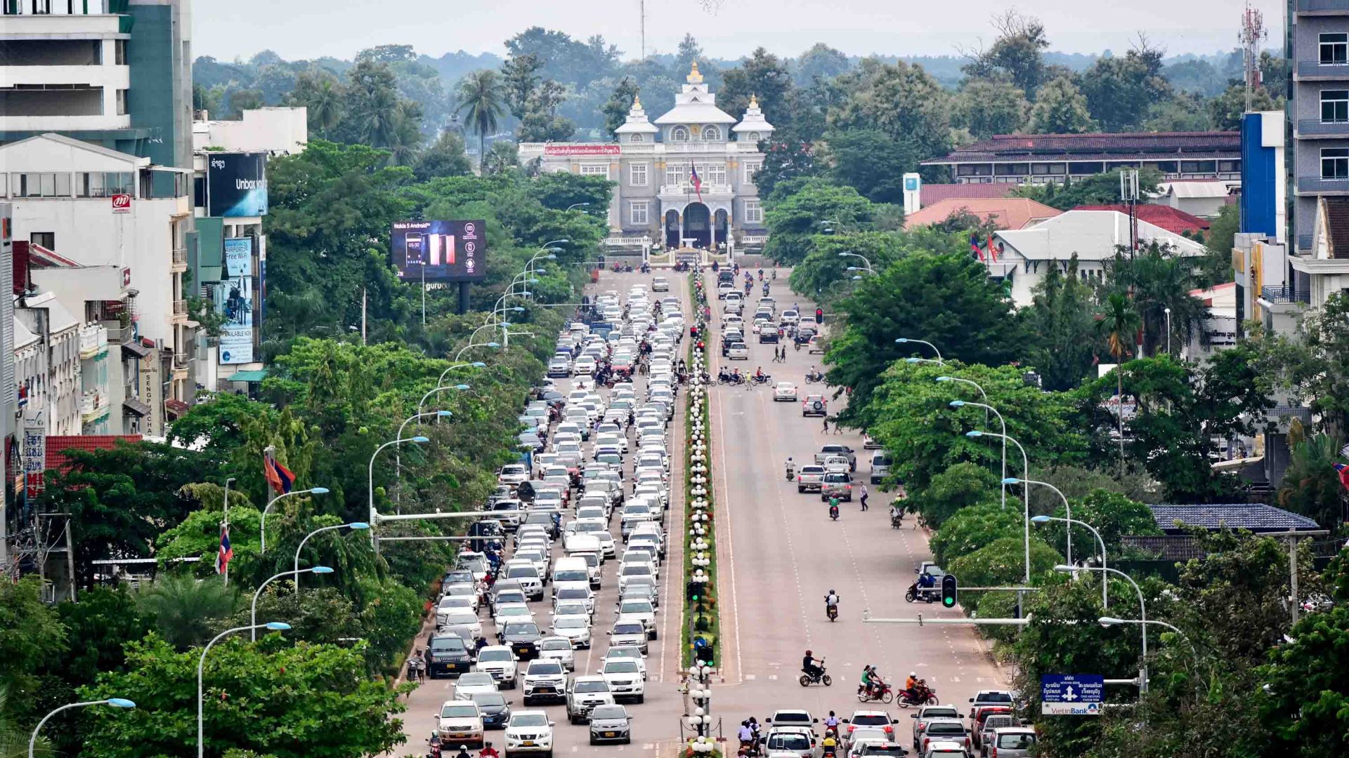 A street in Vientiane, Laos. It has trees on each side and a lot of traffic. The photo is taken from up high, looking down.