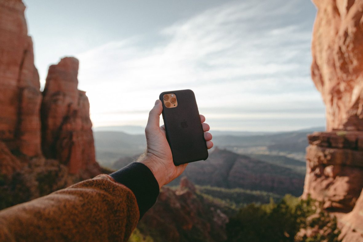 A mountain scene with a hand holding a phone before it.