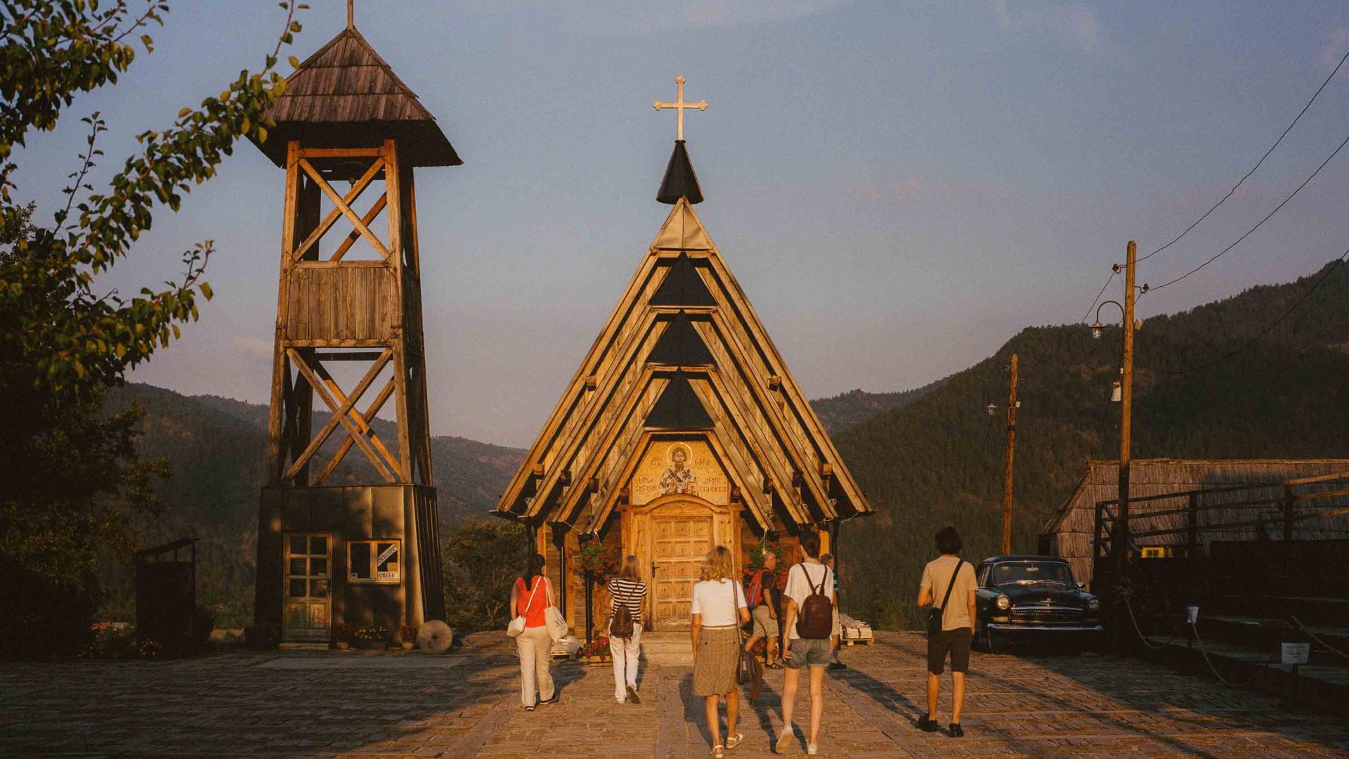 People walk toward the St. Sava Orthodox church, a wooden and triangular structure.