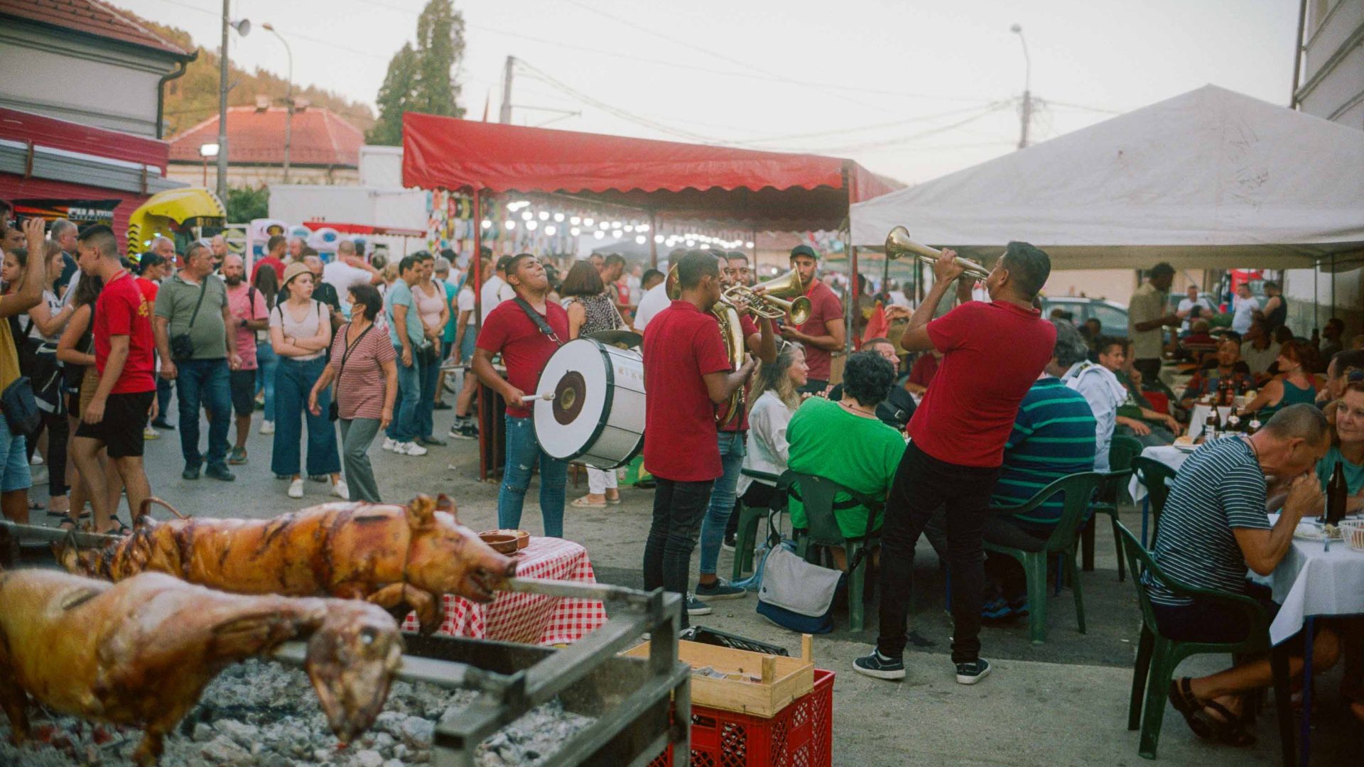 Festivities in the city of Guca. Pigs are roasting, musicians are in the street playing music and people are milling round stalls.