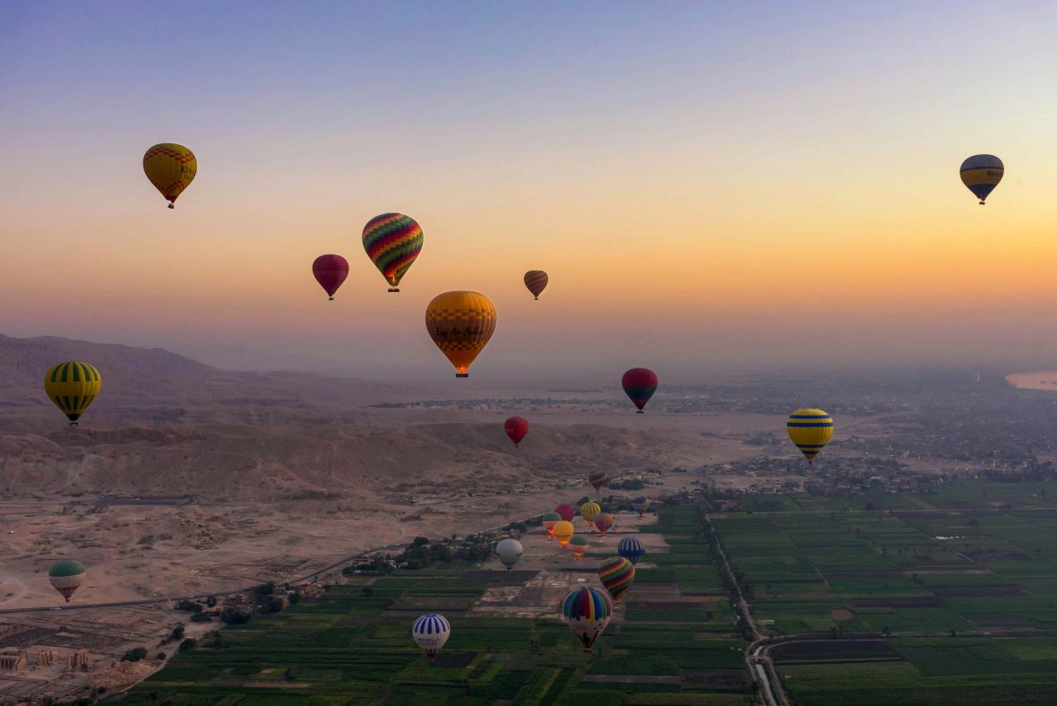 The Valley of the Kings as seen from up high. There is soft light and hot air balloons in the sky.