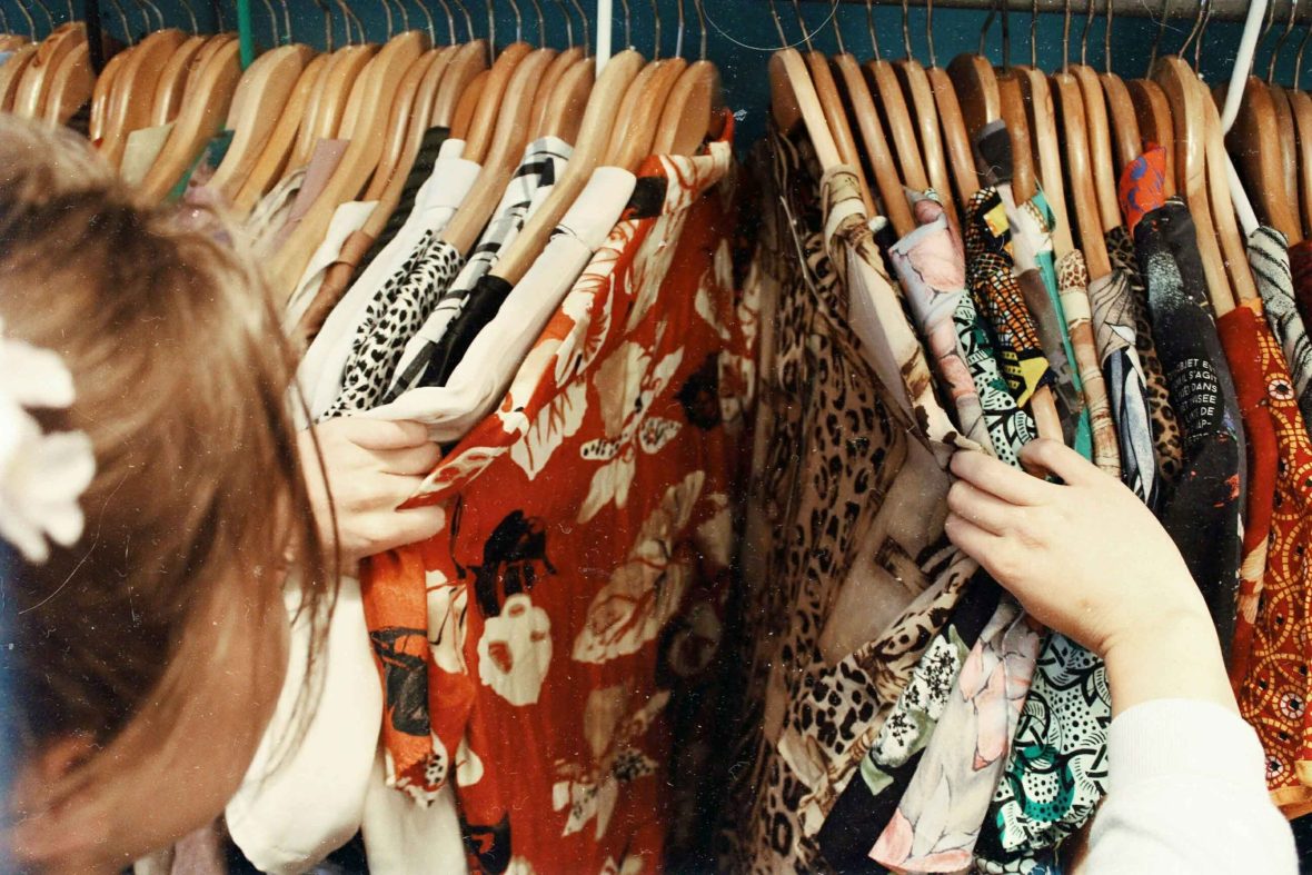 A woman combs through racks of second hand clothes.