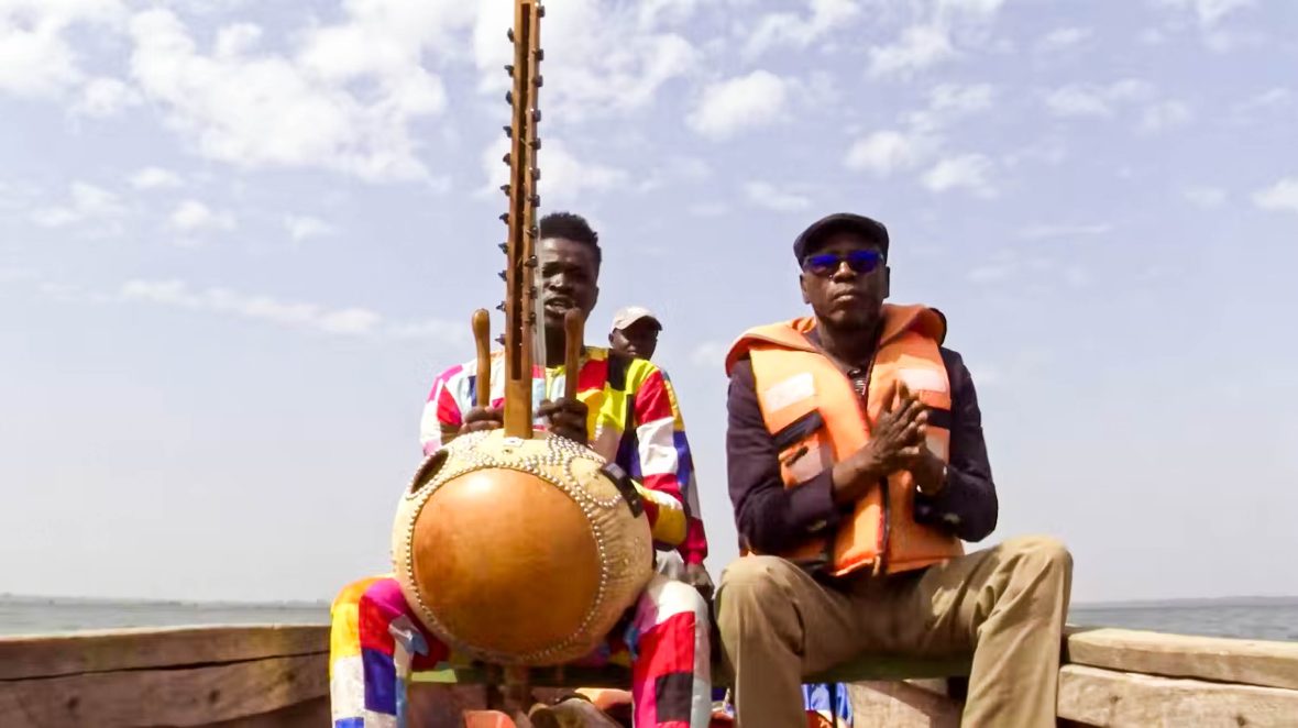 Two men sit side by side. One of them holds the kora.
