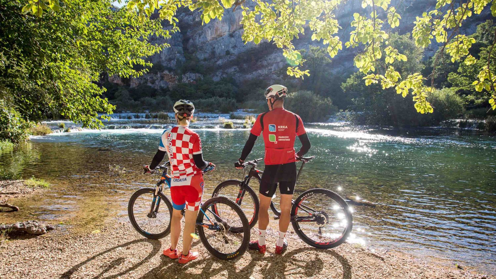 People who have been bike riding in Krka National Park pause to enjoy a view of a waterfall.