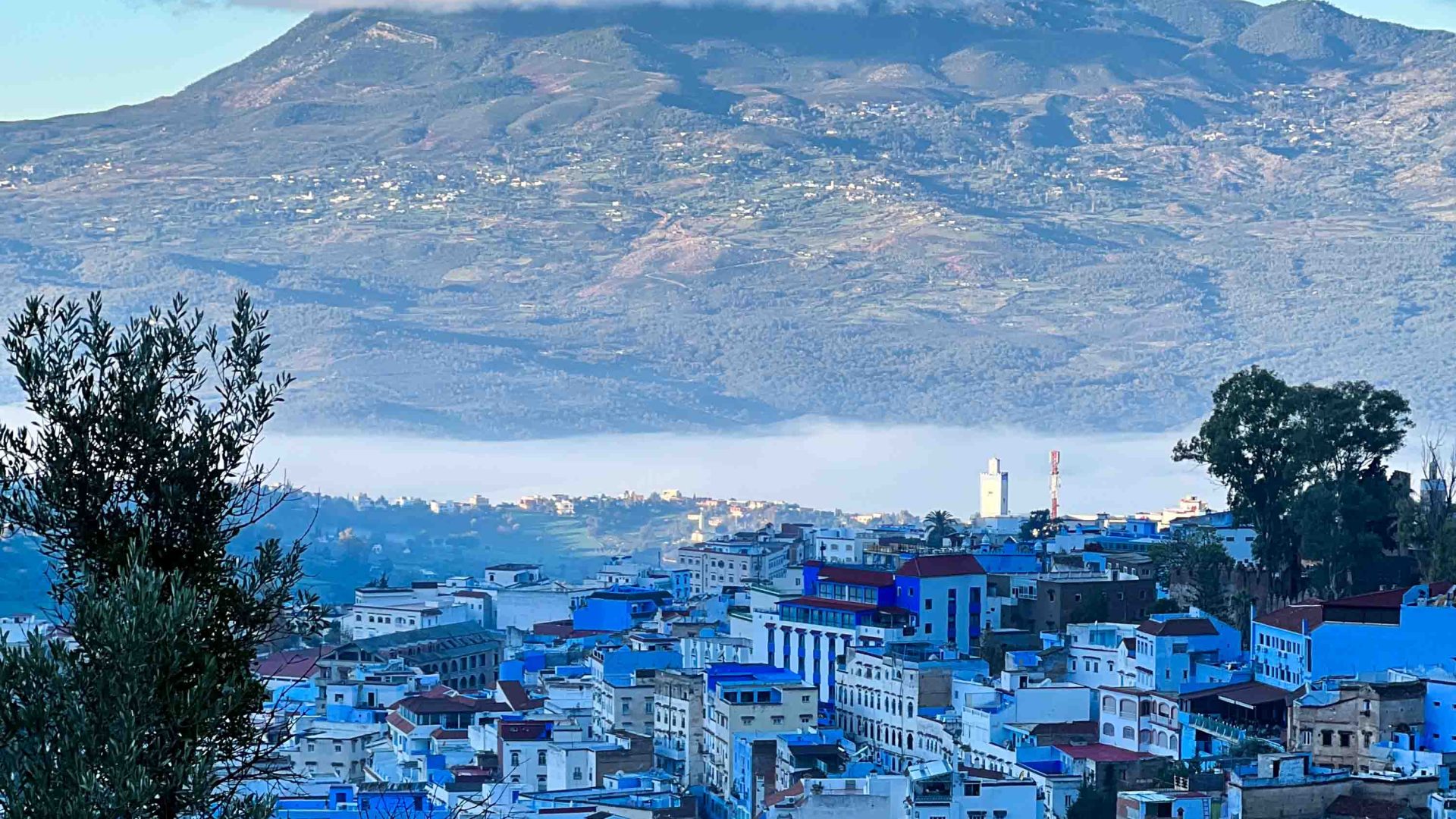 A view from above of the Moroccan town of Sunrise over Chefchaouen with blue roofs by the lake and mountains.