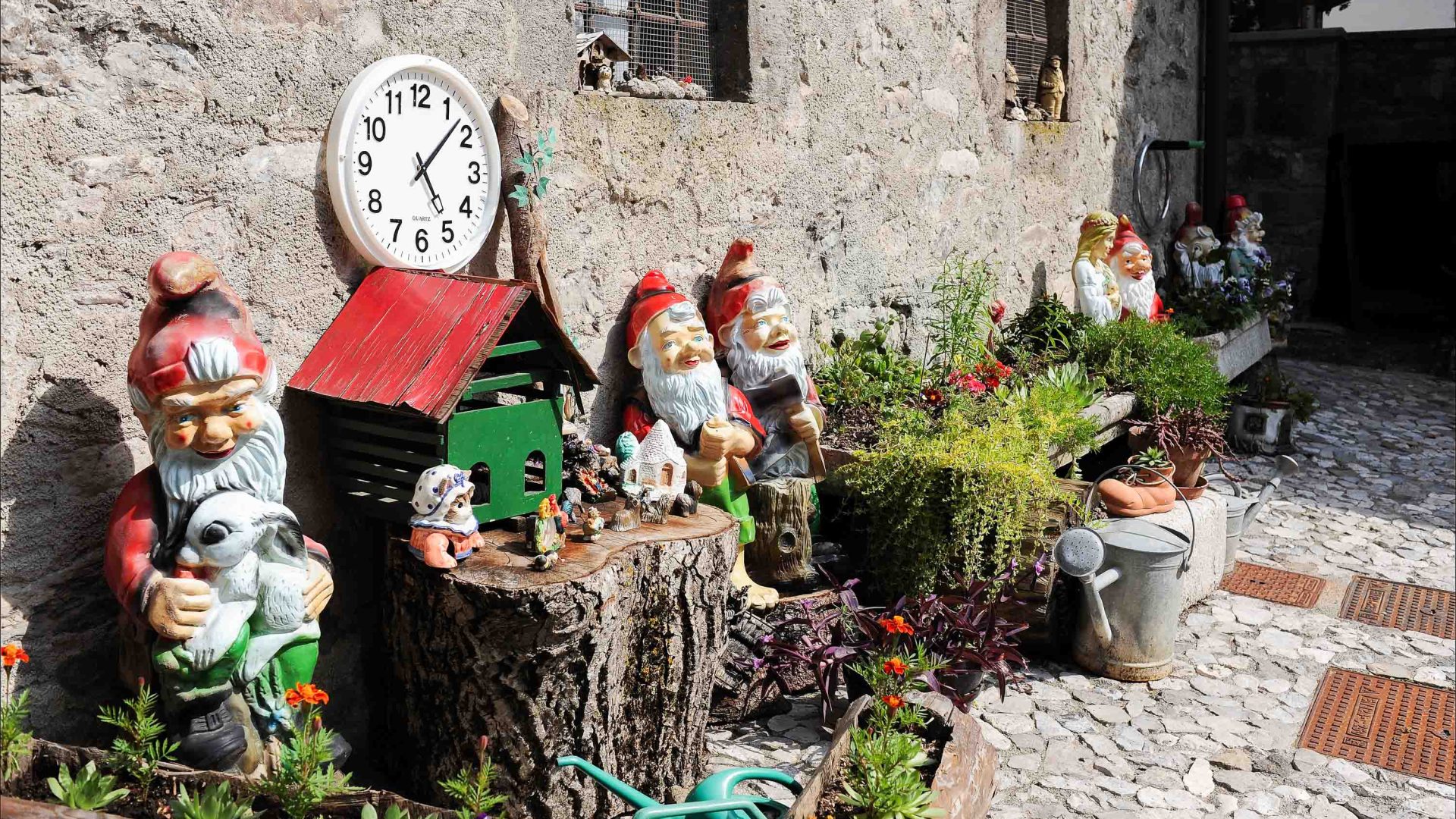 In the town of Pesariis someone has created a garden along their wall filled with gnomes and with a clock sitting on top.