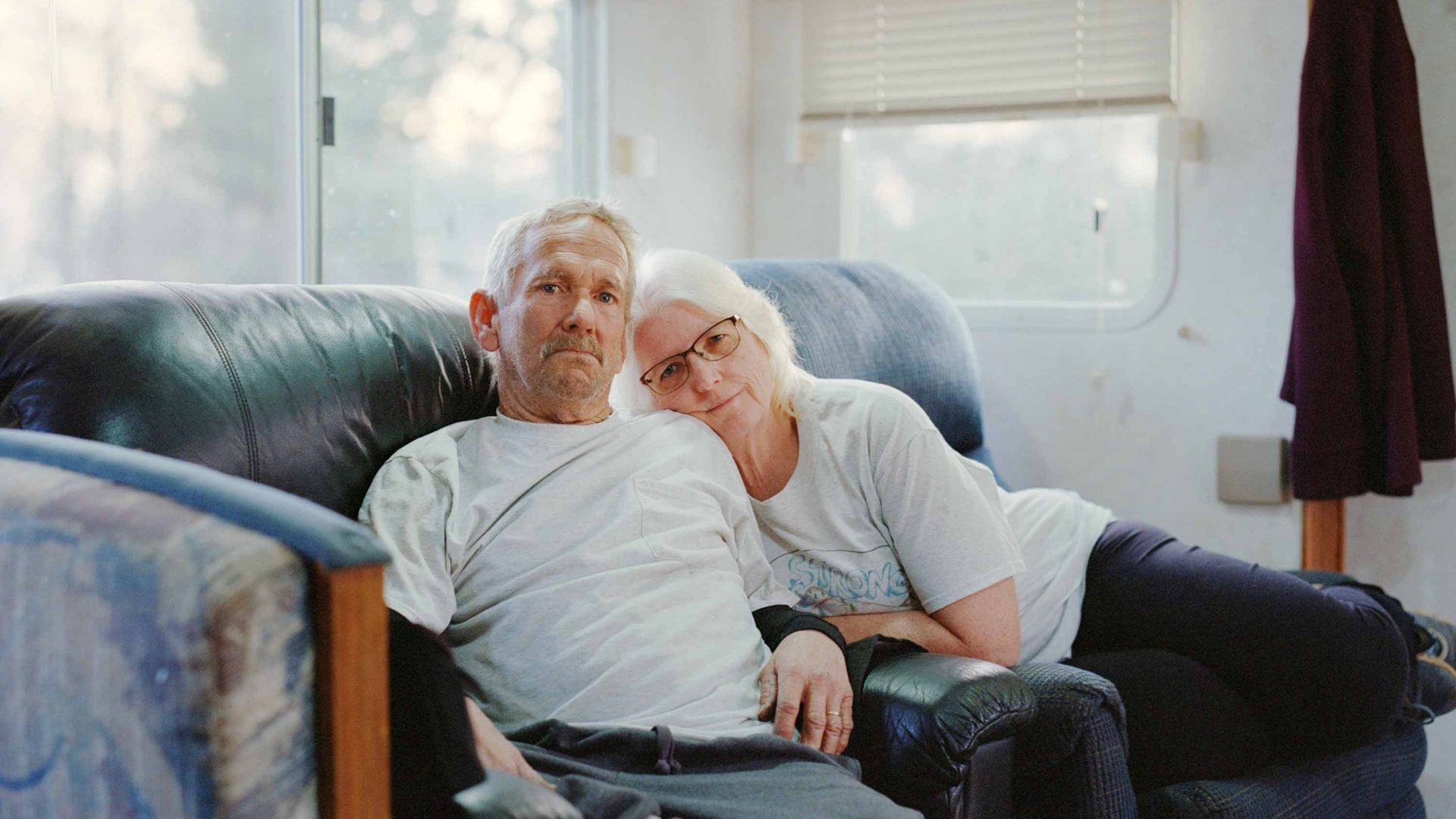 A portrait of two people in a caravan. A woman has her head resting on a mans shoulder.
