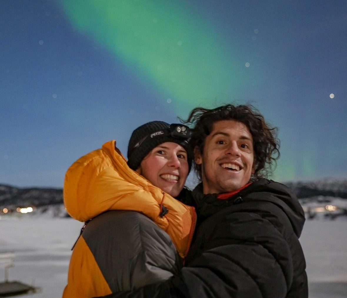 A couple stand in front of a green Aurora sky.