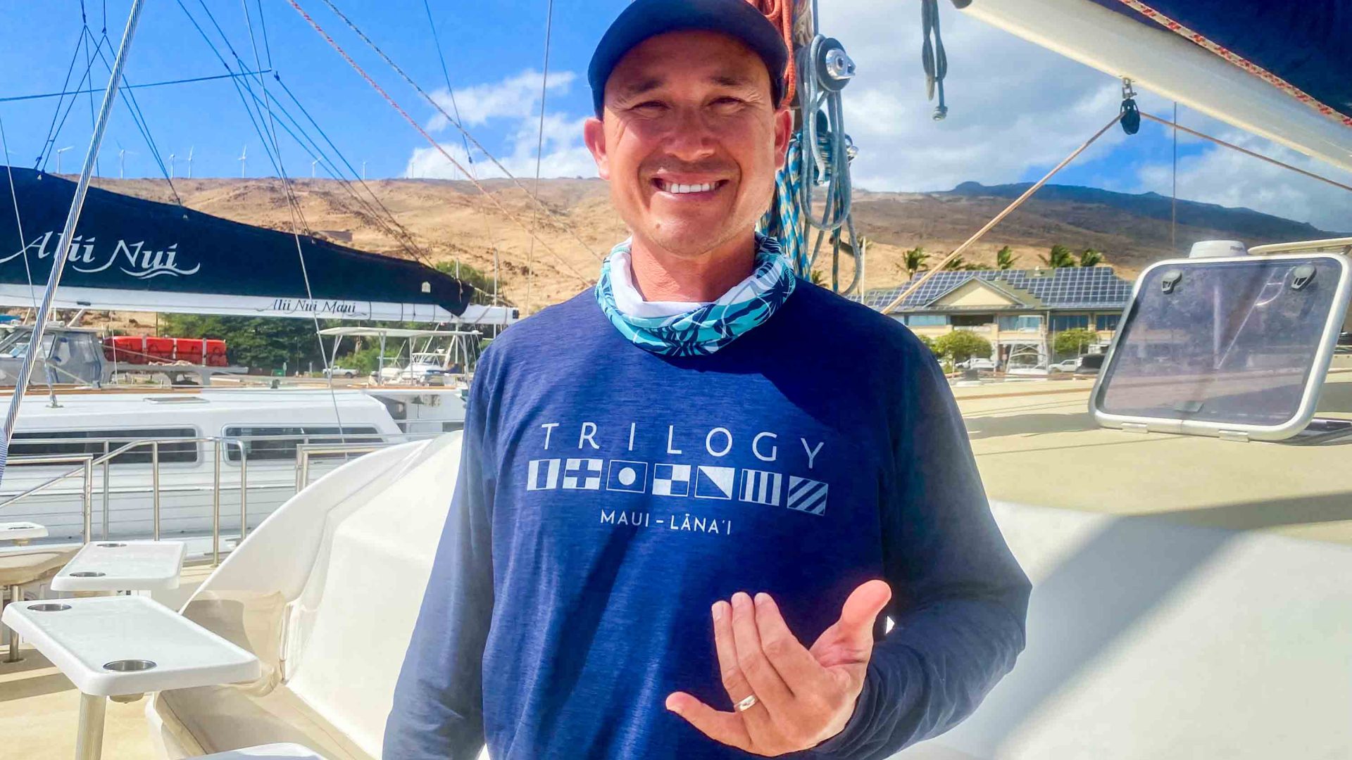 Riley wears a blue t shirt and smiles to camera. He is on a boat and wears a cap.