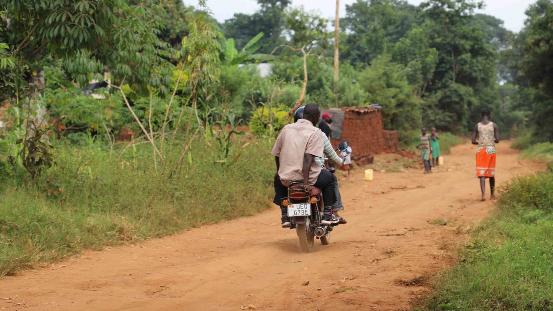 A motorcycle transports a passenger up a dusty road.