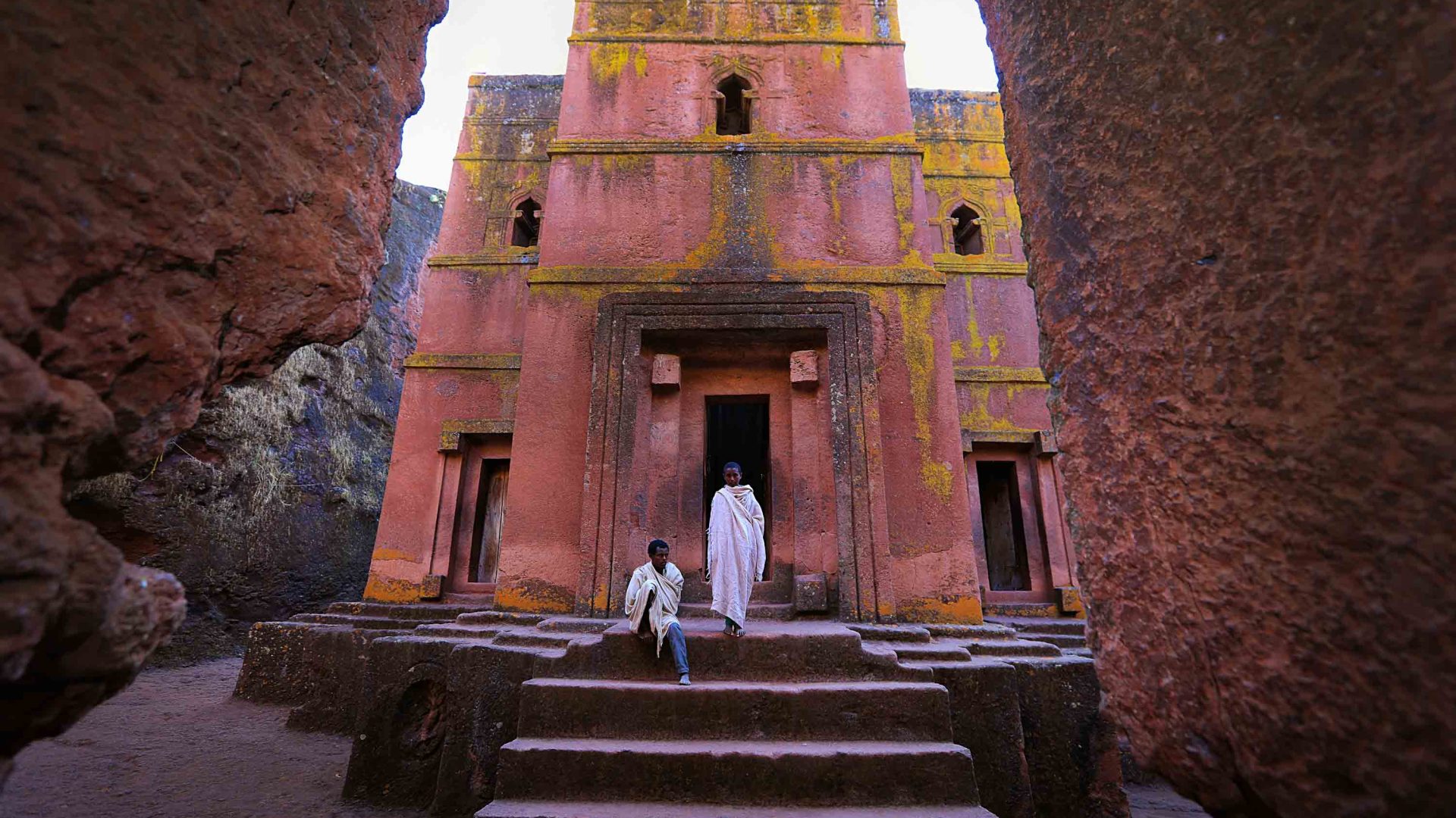 Two men in white clothes stand on the steps of an old church.