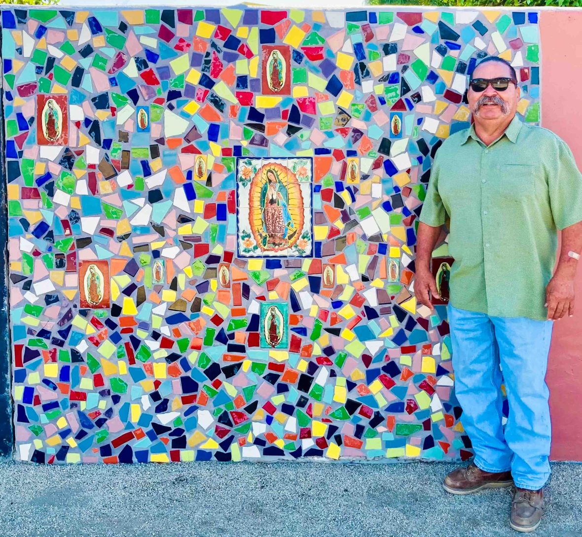 Ruben Gonzales smiles in front of the Virgen de Guadalupe, a coloful mosaic that he made in Coachella.