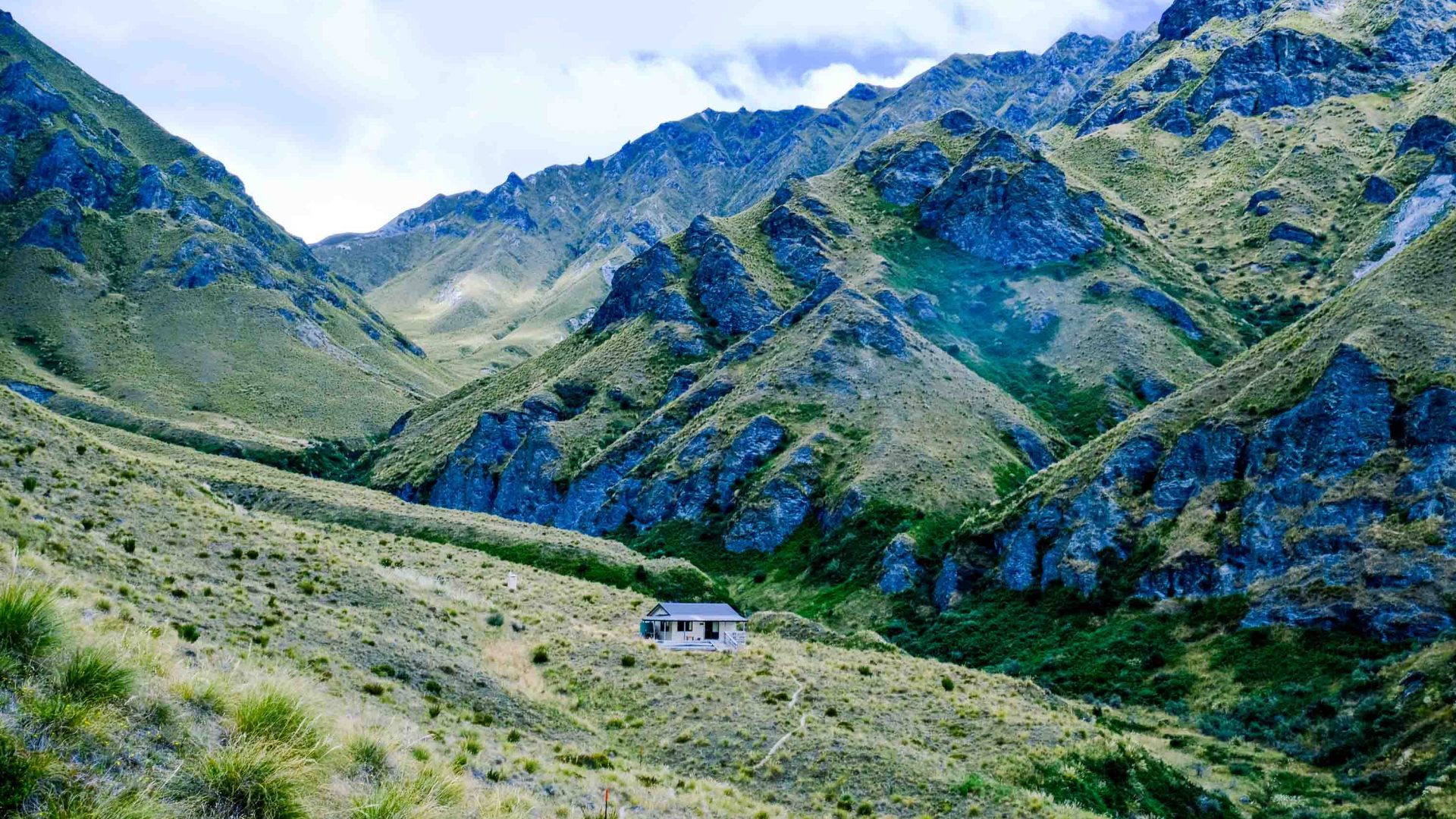 A back country hut surrounded by green mountains.