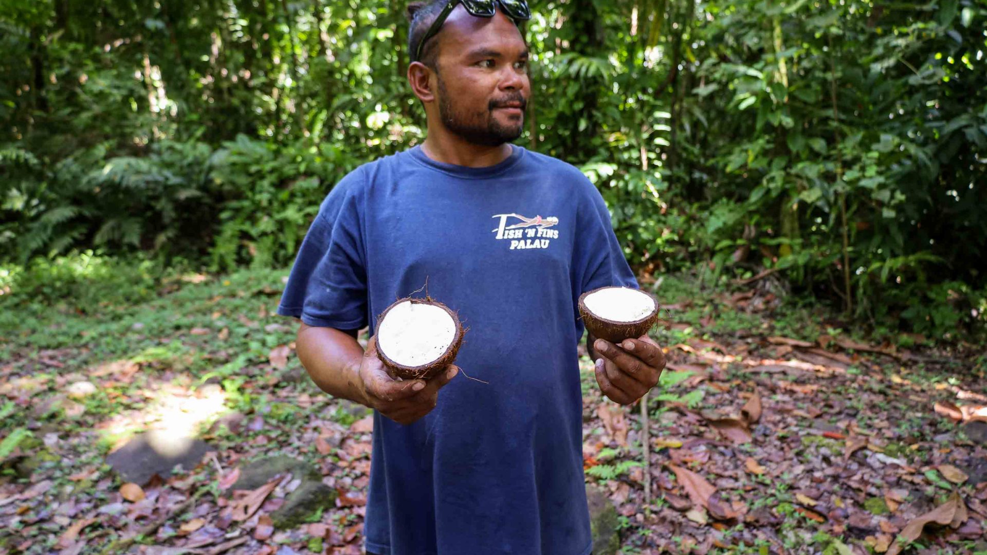 A man holds two halves of a coconut.