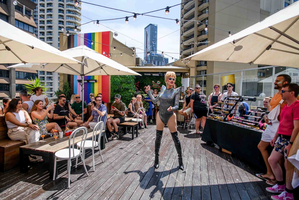 A drag queen entertains a crowd of people on a rooftop.