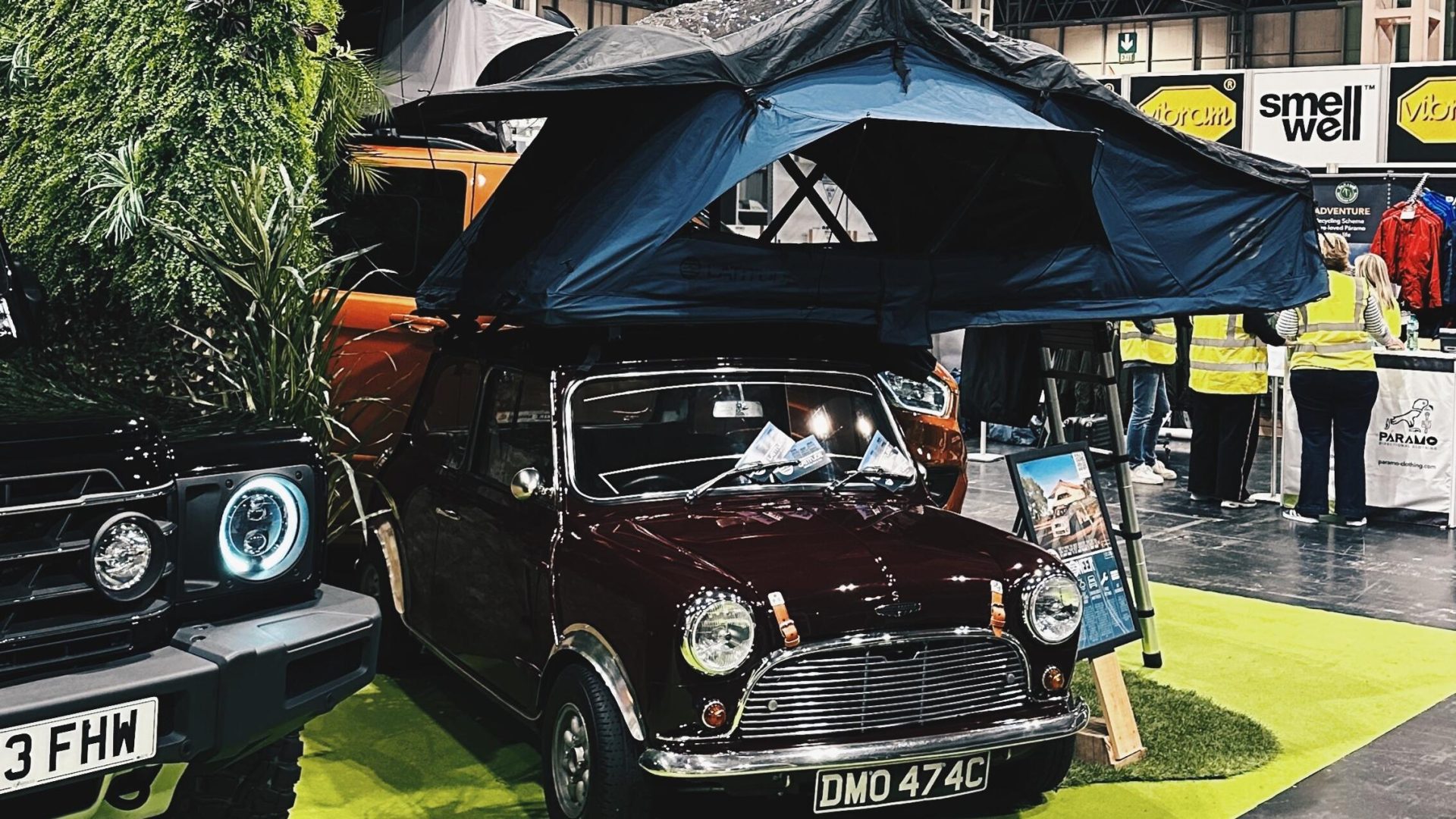 A blue rooftop tent is open on top of a vintage red Mini Cooper.
