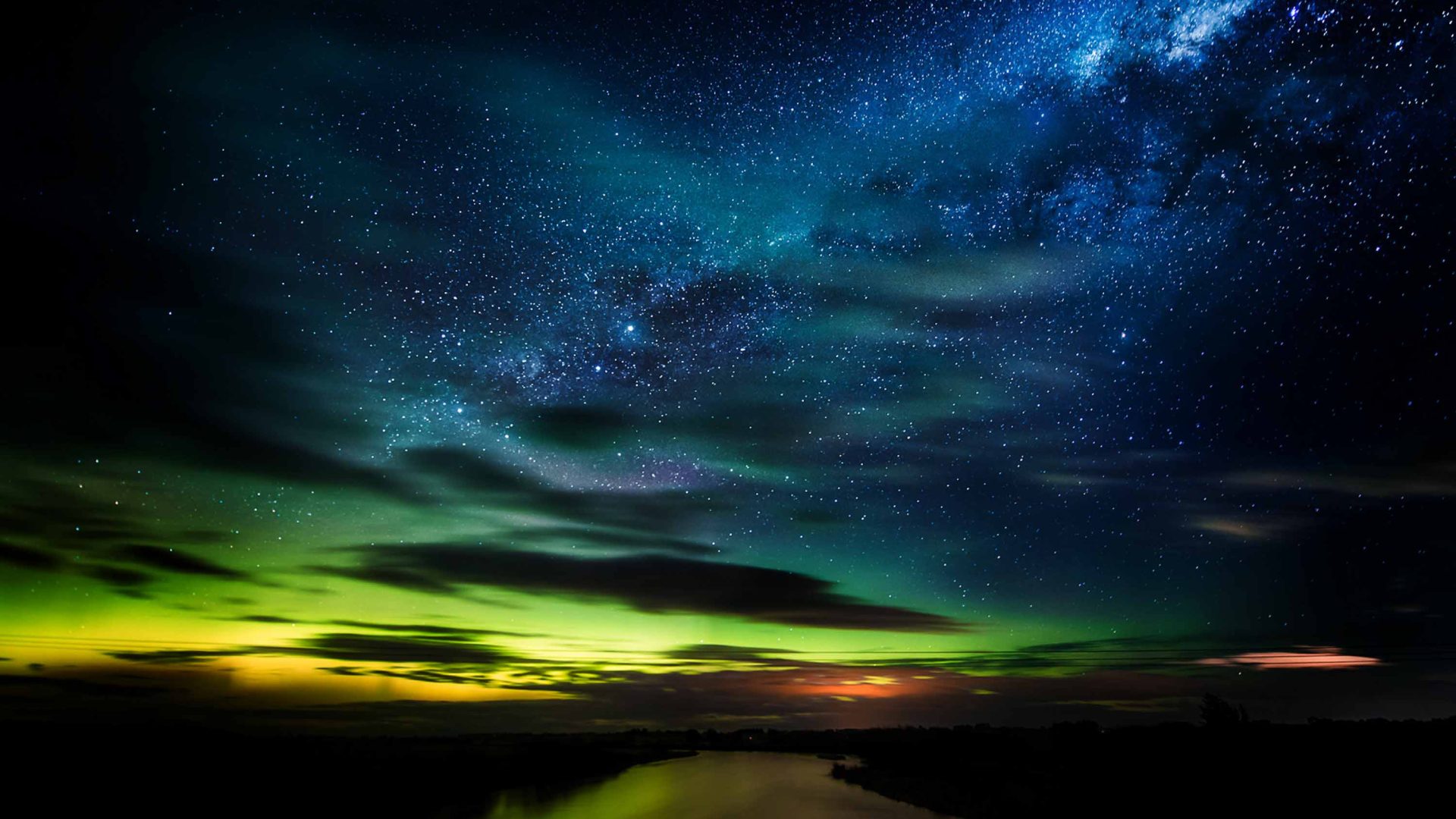 Blue and green star studded sky above a lake.