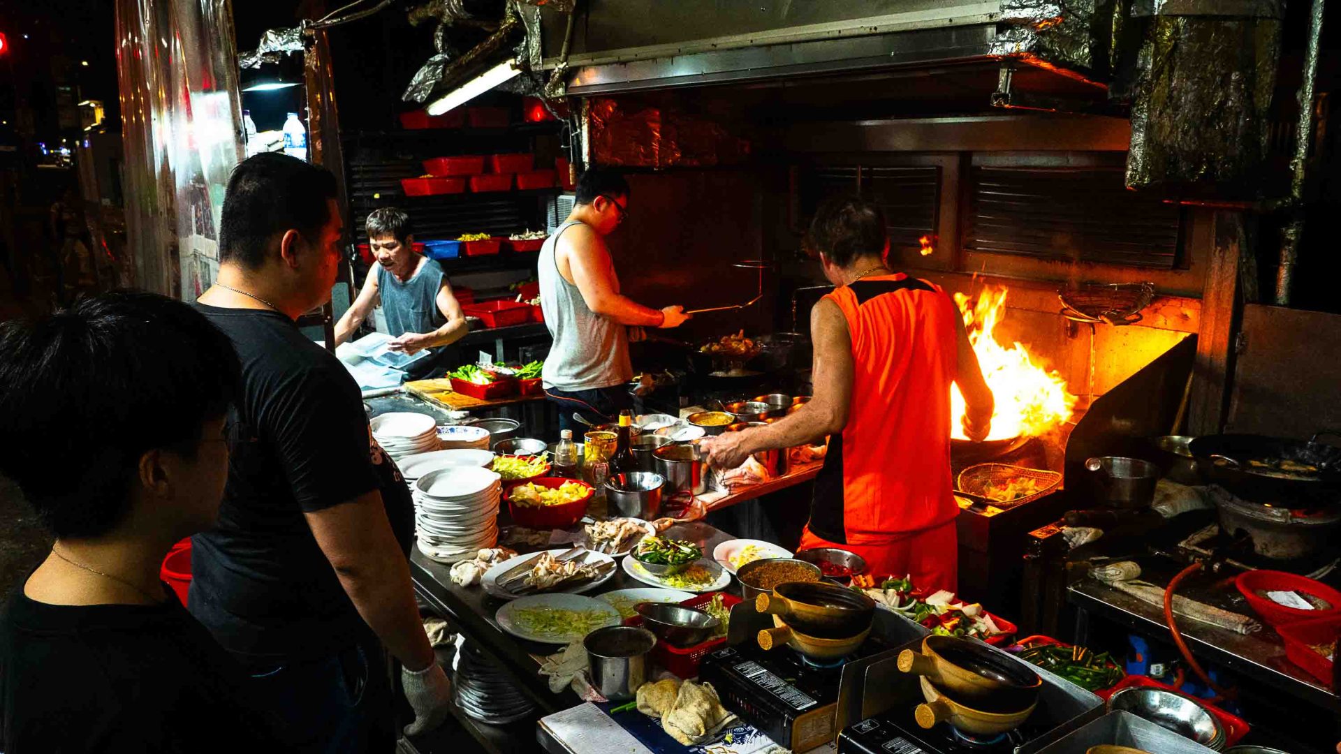 Chefs prepare food in a crowded outdoors kitchen.
