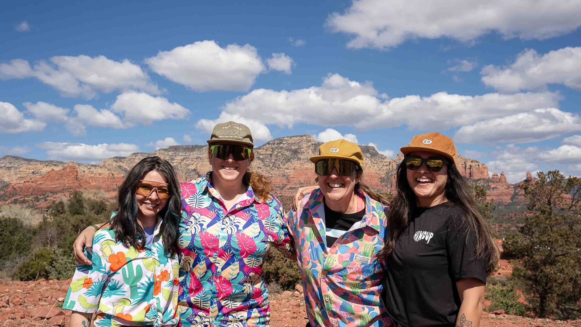 A group of four women smile for a photo. Three wear bold and colorful shirts.