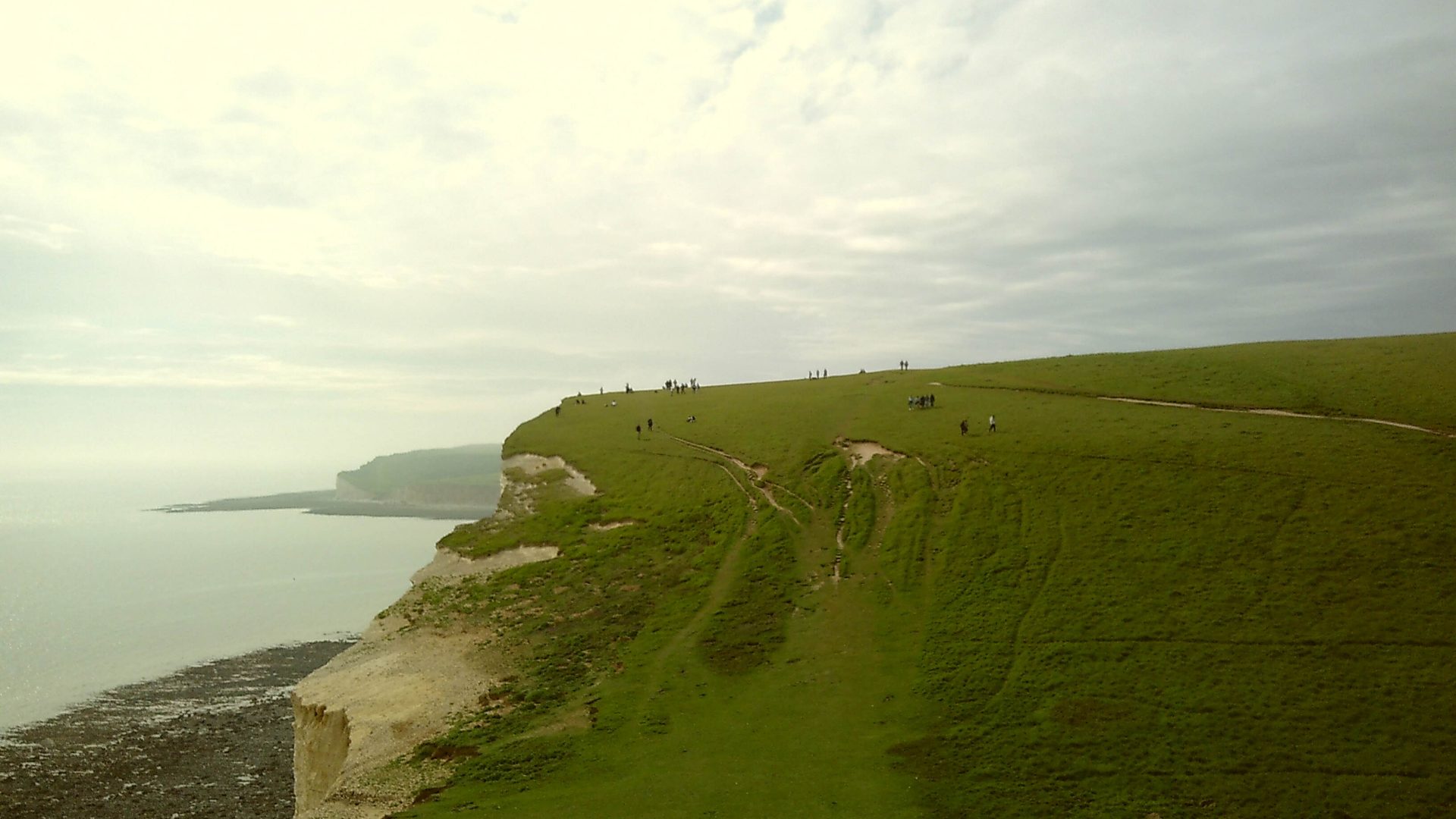 An overcast view of steep, green hills atop white chalk cliffs.