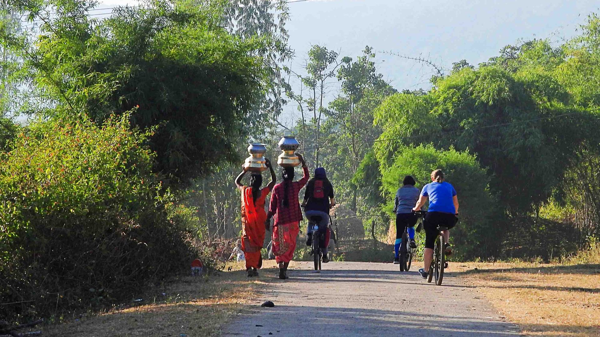 The group cycles past a few women carrying pots on their heads.