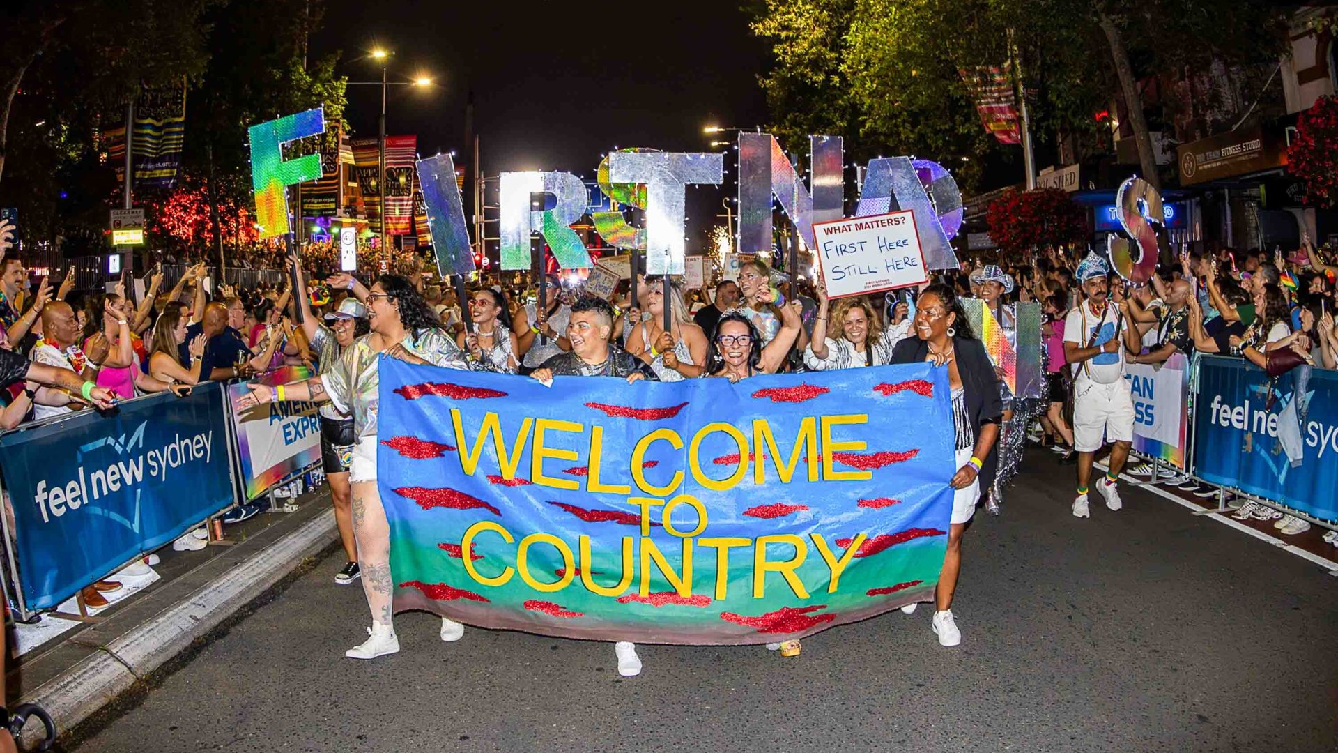 A First Nations group marches in the Sydney Mardi Gras. They hold a banner that reads 'Welcome to country'.