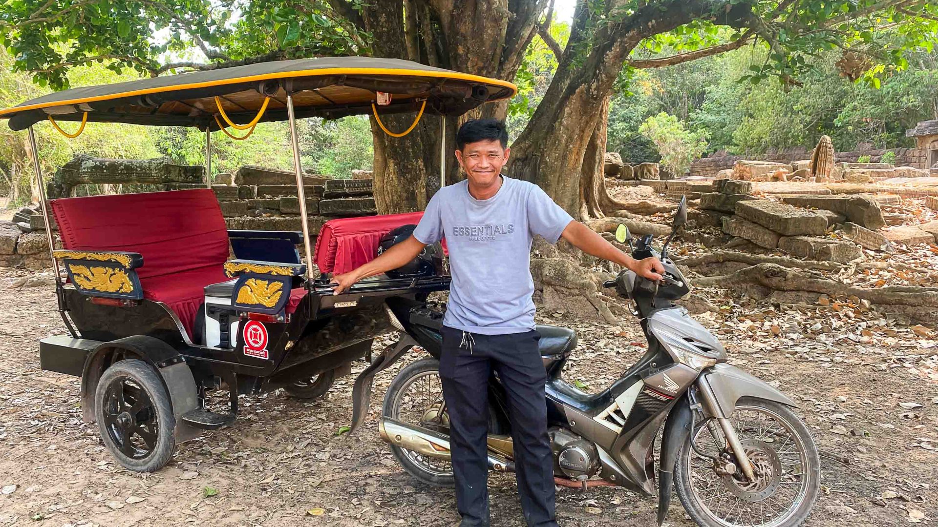 Sour with his tuk tuk. He stands under a tree.