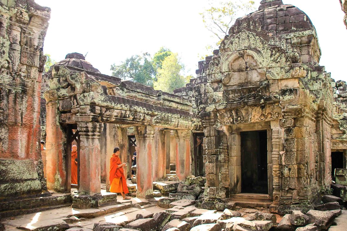 Monks in orange robes walk through a temple at Angkor Wat.