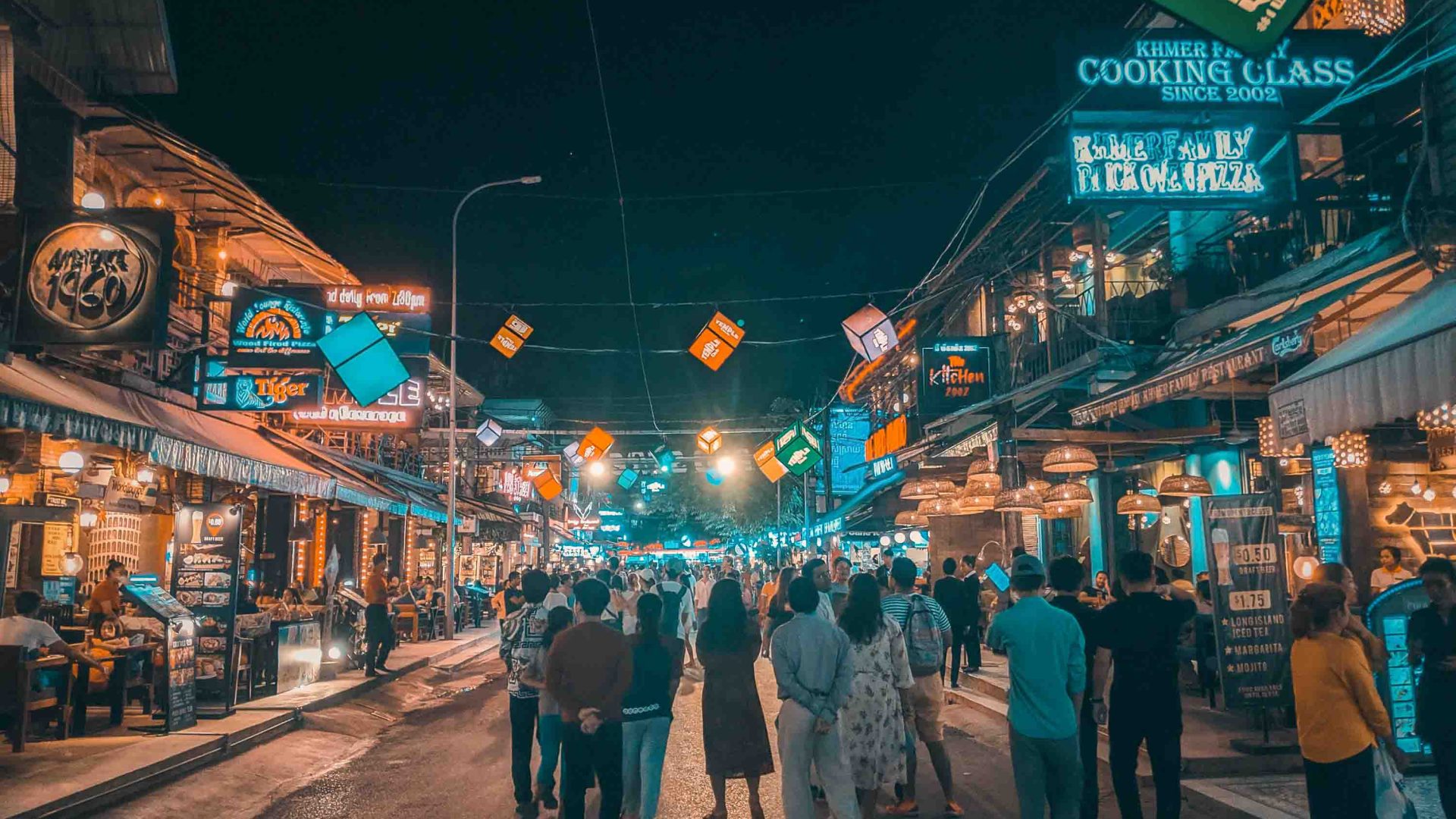 Pub Street in Siem Reap teems with tourists. It is lit up with lots of lights and people walk down the street.