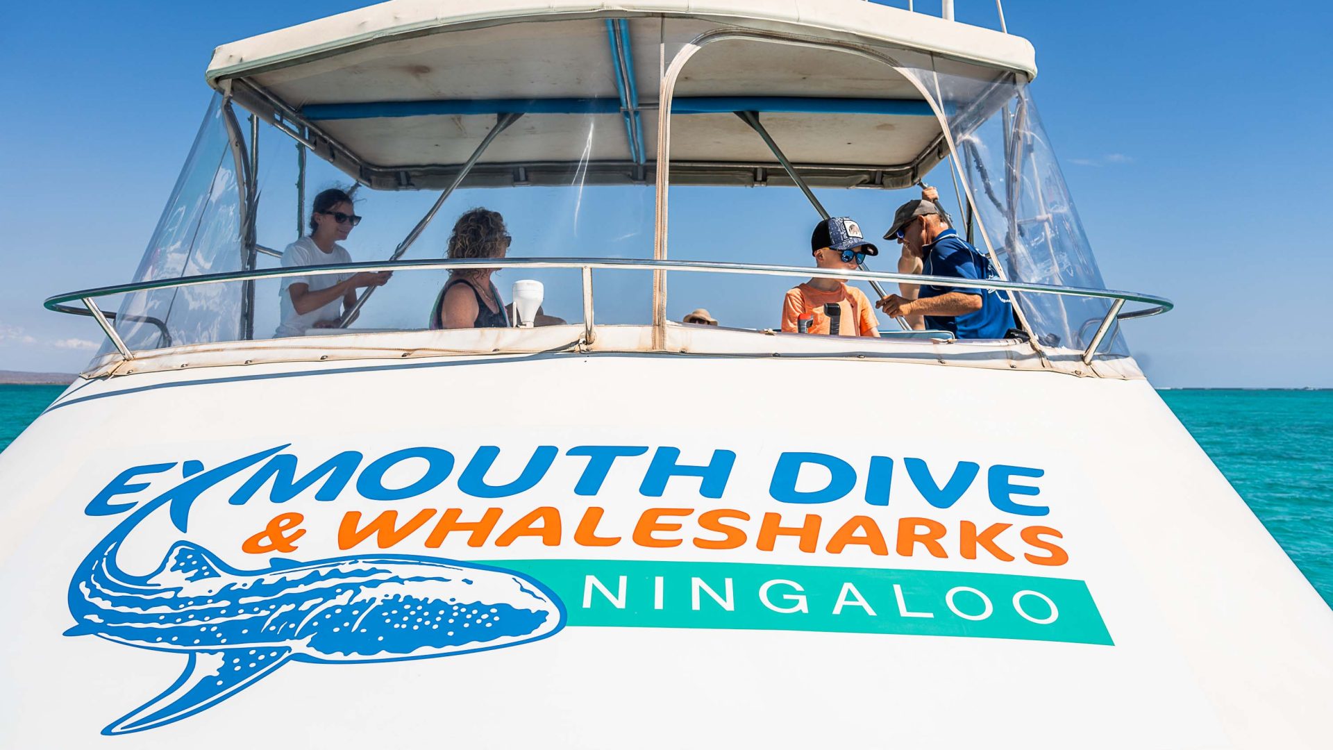 A boat with people on it. The front of the boat is branded with the name Exmouth Dive and whale shark Ningaloo.