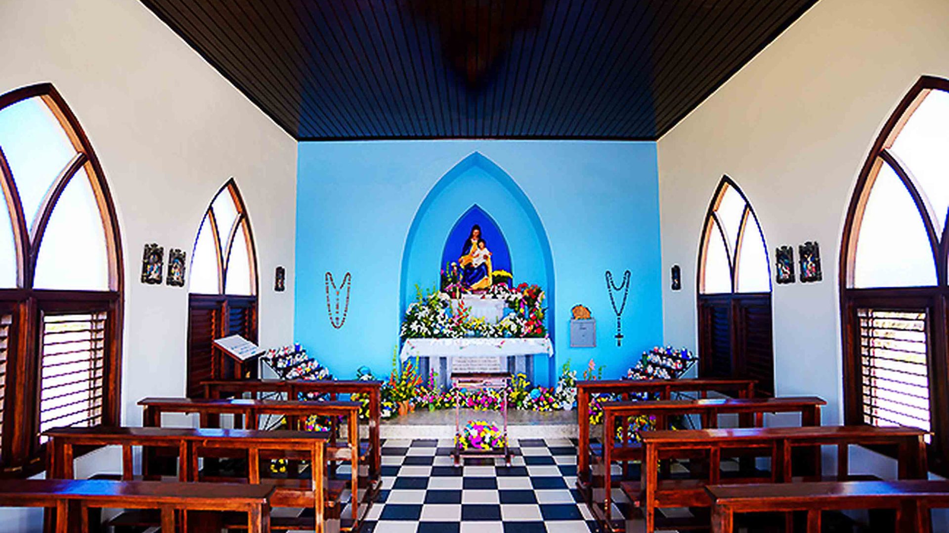 Alto Vista Chapel with pews, black and white floor tiles and a blue wall.