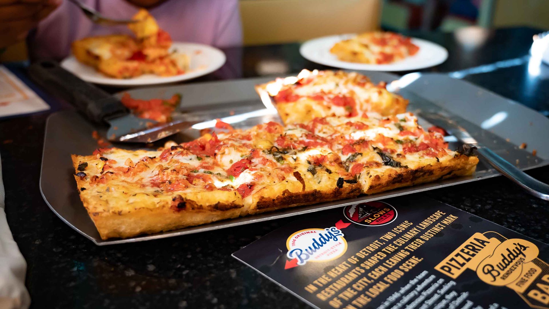 A tray of pizza above a branded Buddy's pizza box.