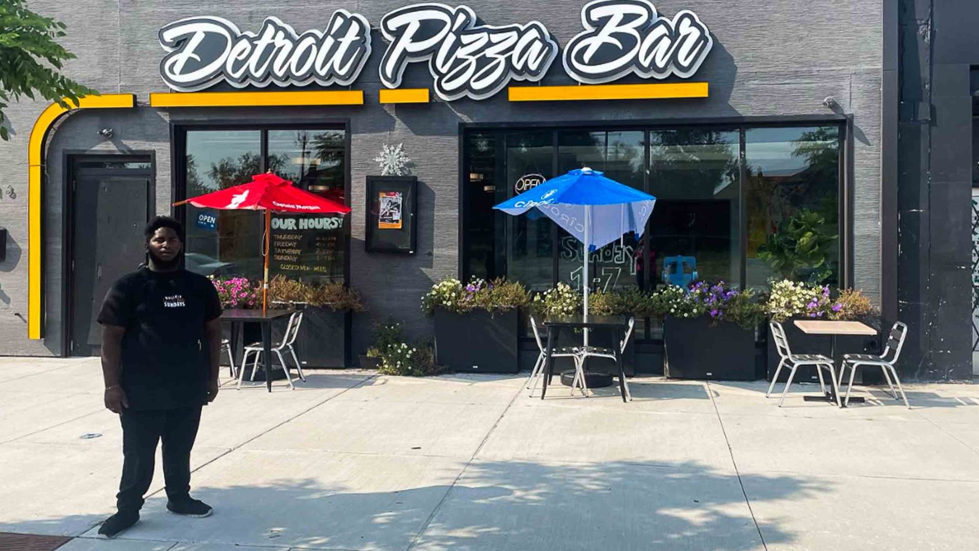 A man stands out the front of a pizza bar.