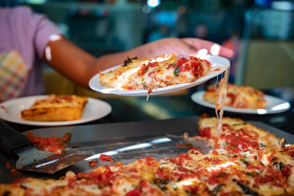 A hand holds a plate with slices of pizza.