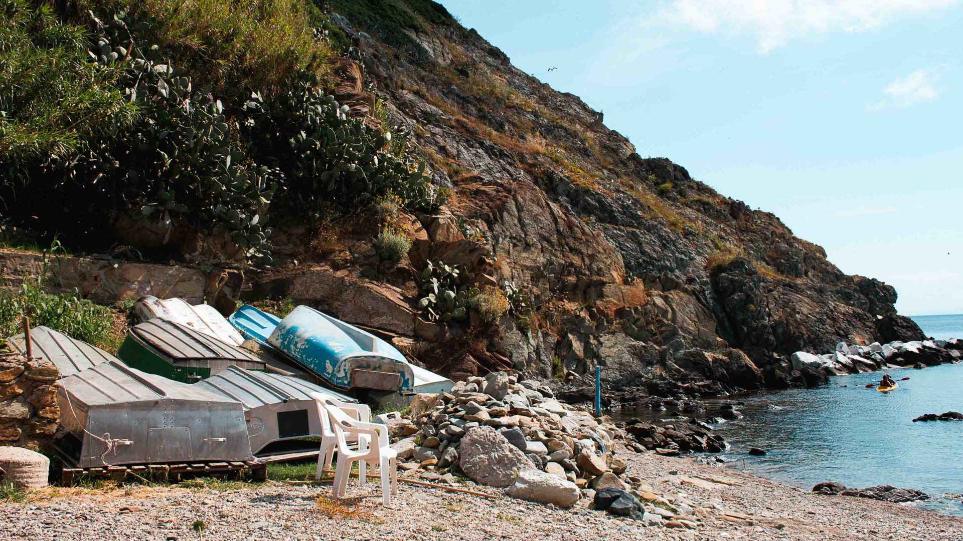 A beach with row boats upturned on the shore and kayakers in the water.