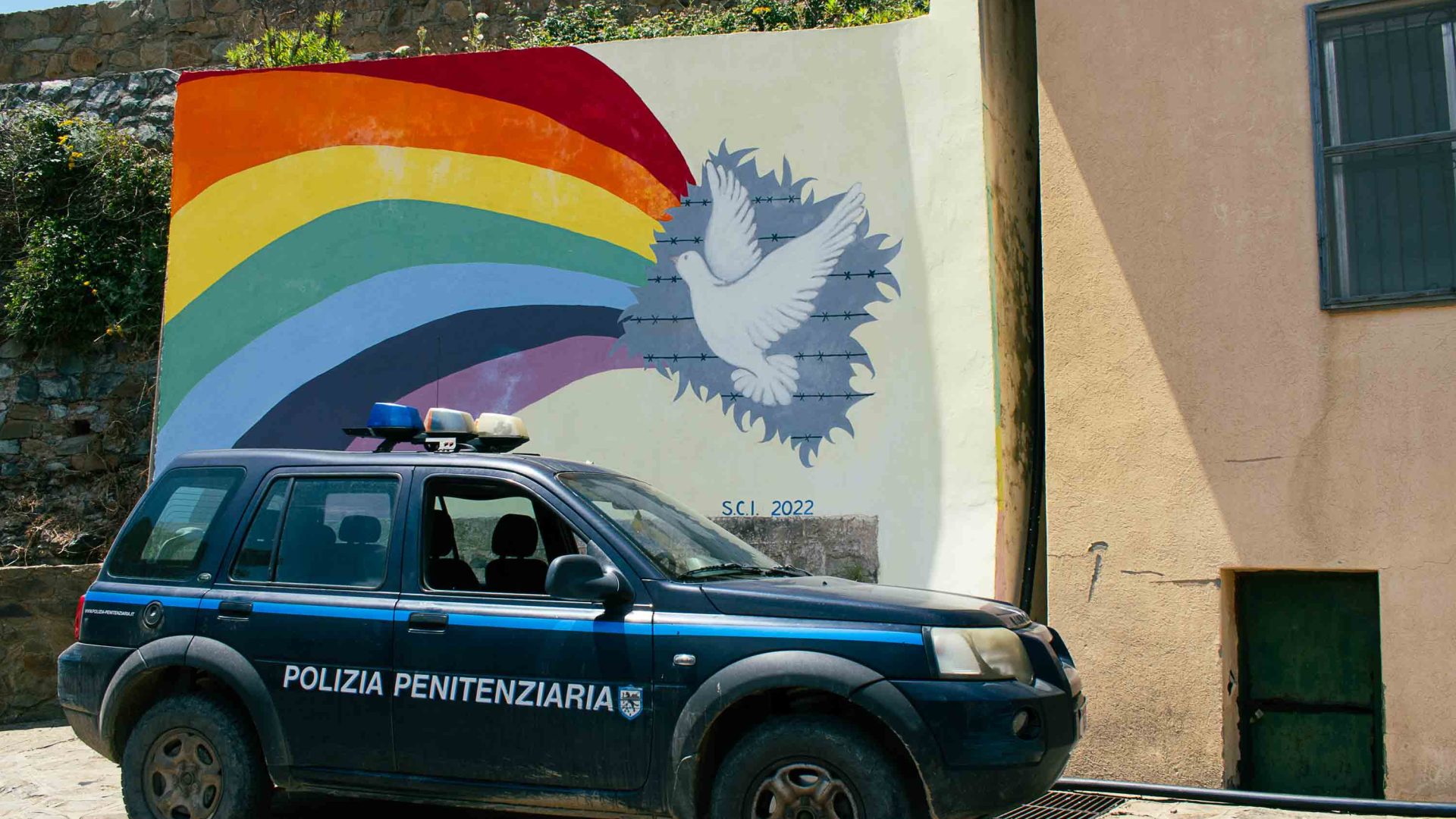 A mural of a rainbow and peace dove alongside a police vehicle.