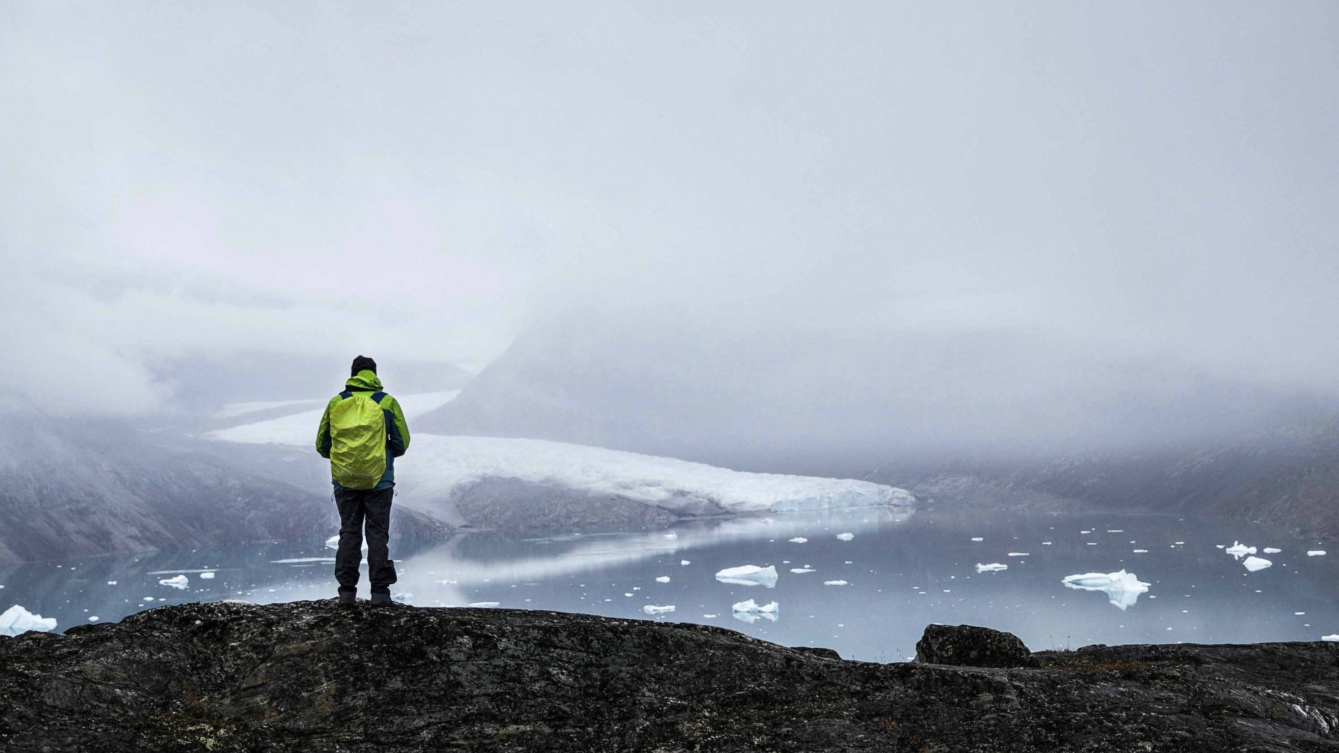 A tourist looks out over icebergs in Greenland.