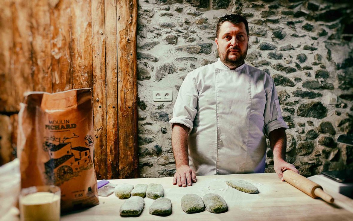 A portrait of a man standing at a bench covered with flour and food he is preparing.