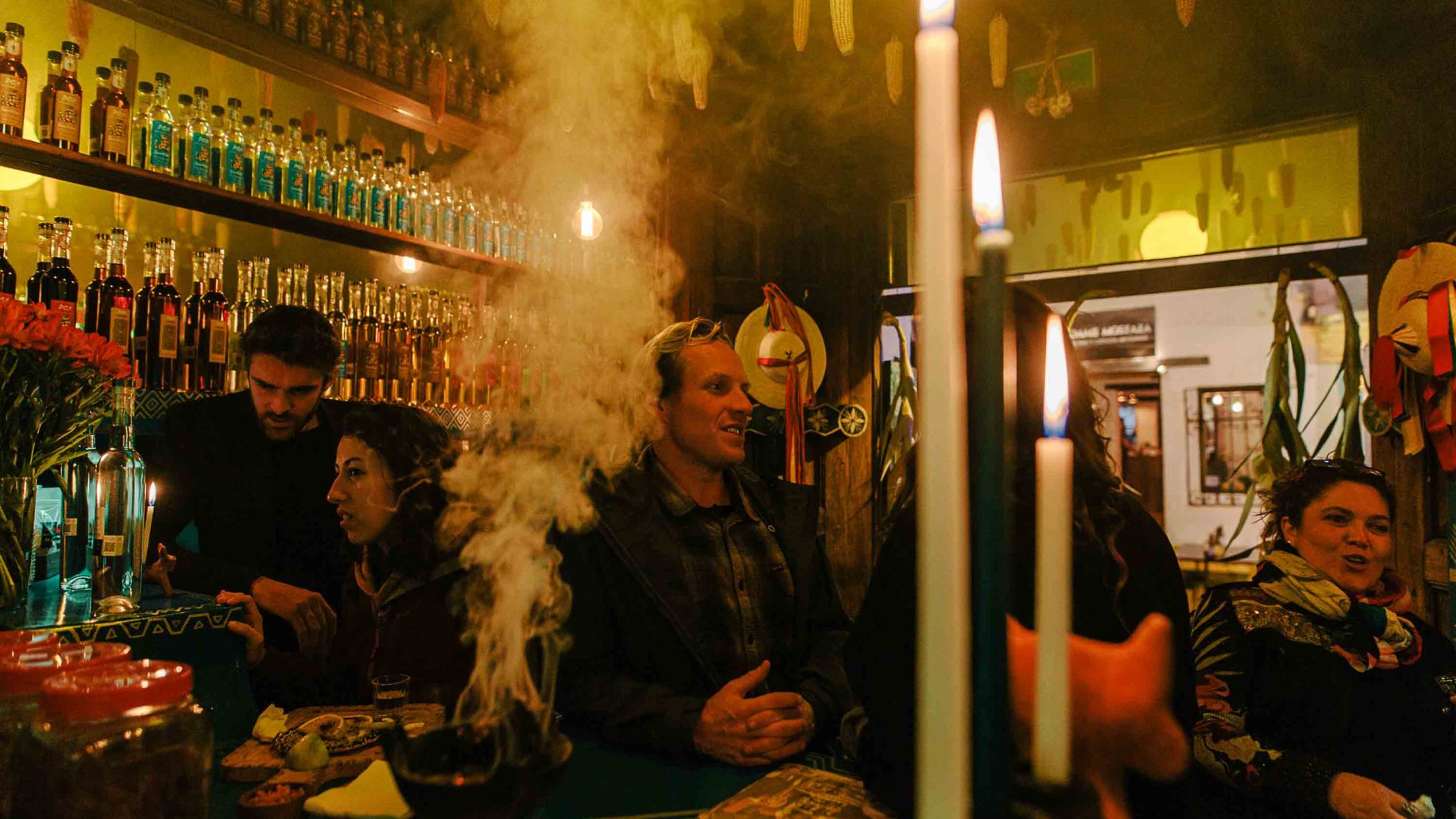 People drink together in the dim lighting of Posheria. Smoke rises from the table.