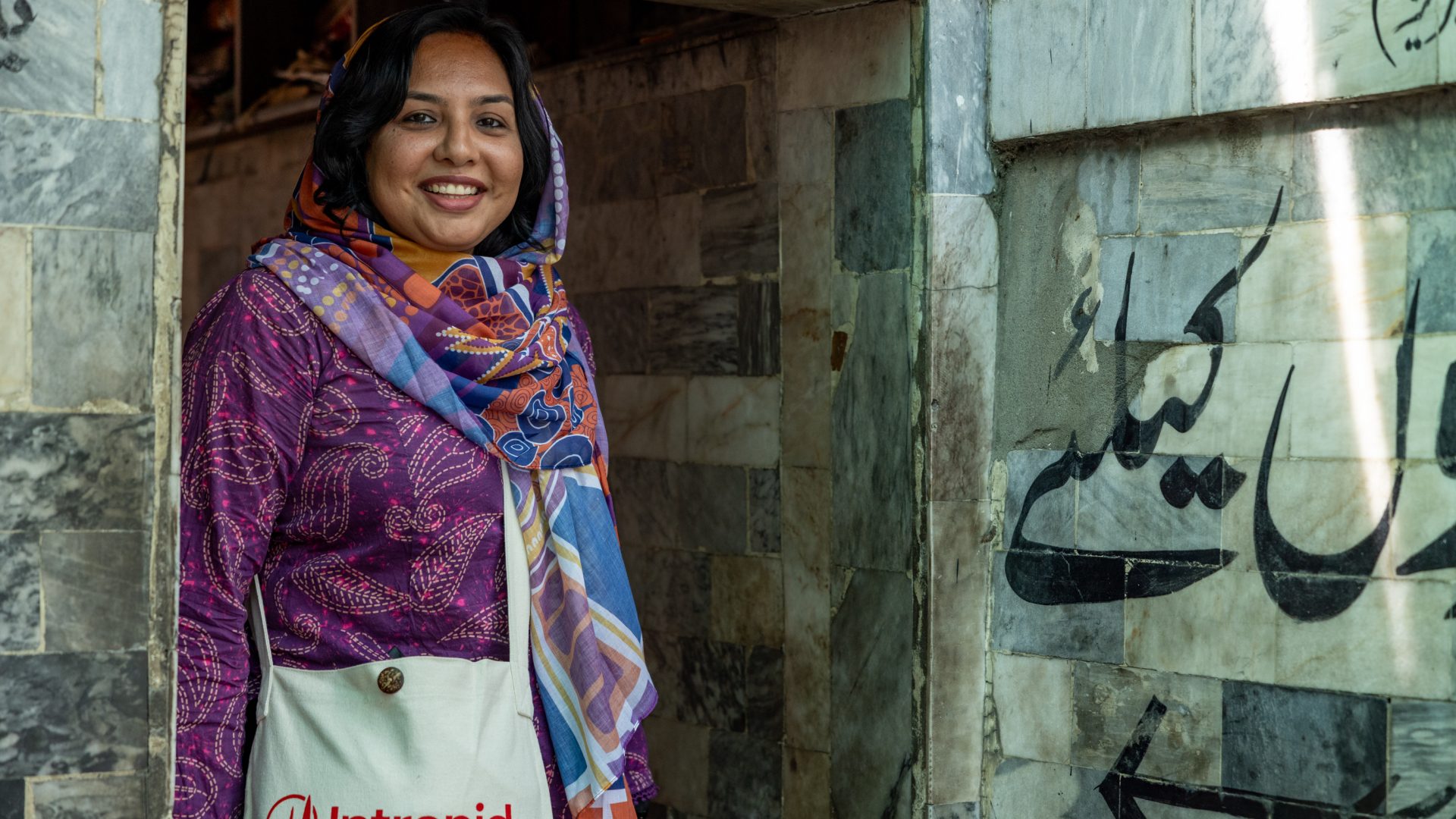 A woman in a bright purple top and patterned scarf smiles to camera