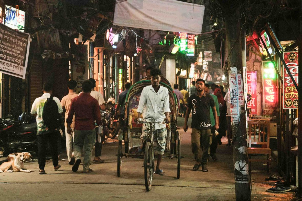 A bustling street at night with a cycle rickshaw in the foreground.