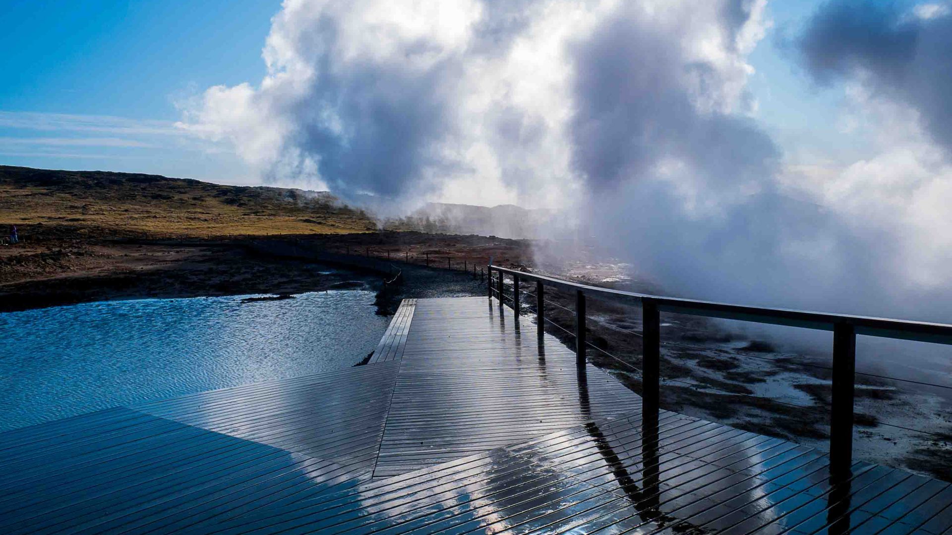 An geothermal pool with steam rising alongside it.