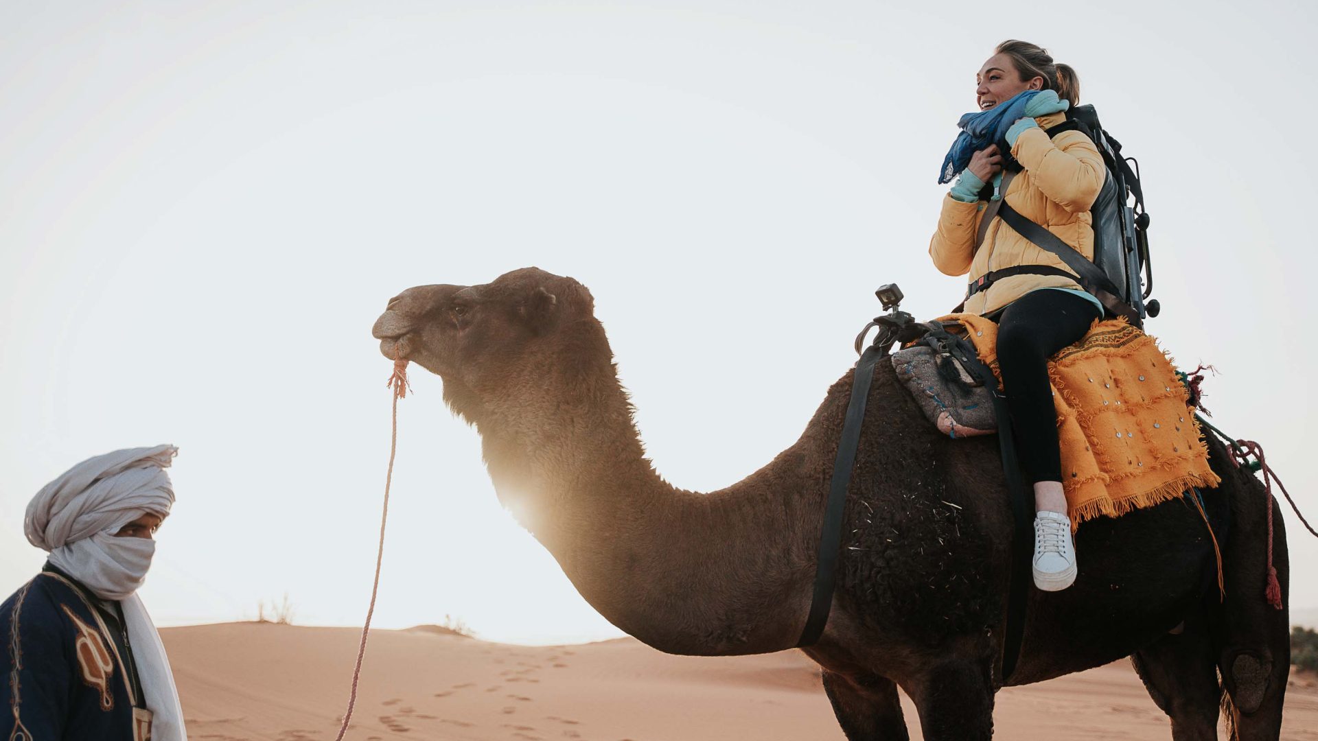 A woman riding a camel in the Sahara on an adapted saddle.