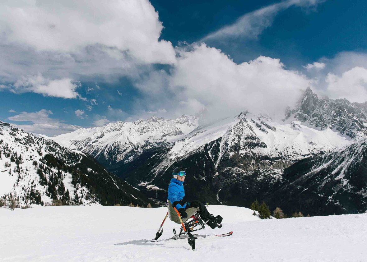 A woman on the top of a snowy mountain in a chair adapted for skiing.