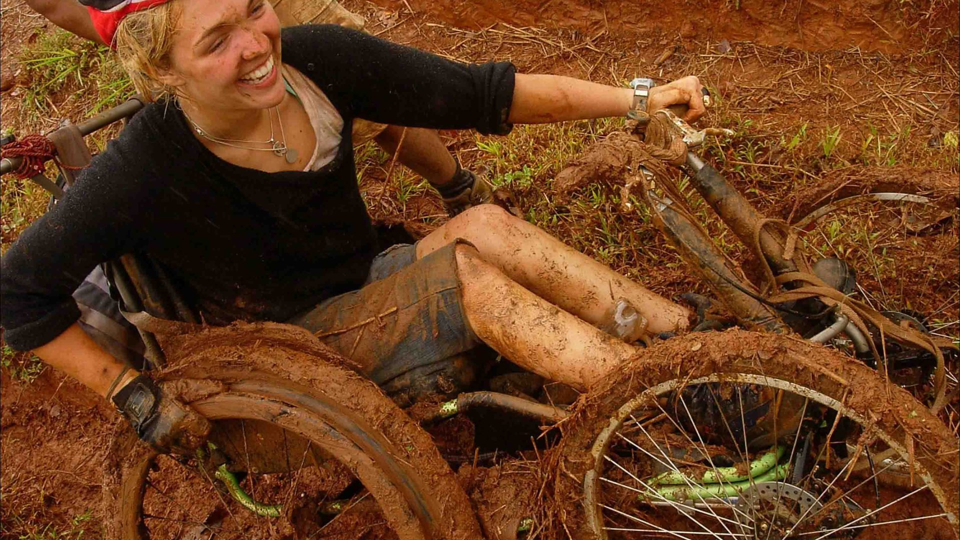 A woman pushing her wheelchair through thick mud.