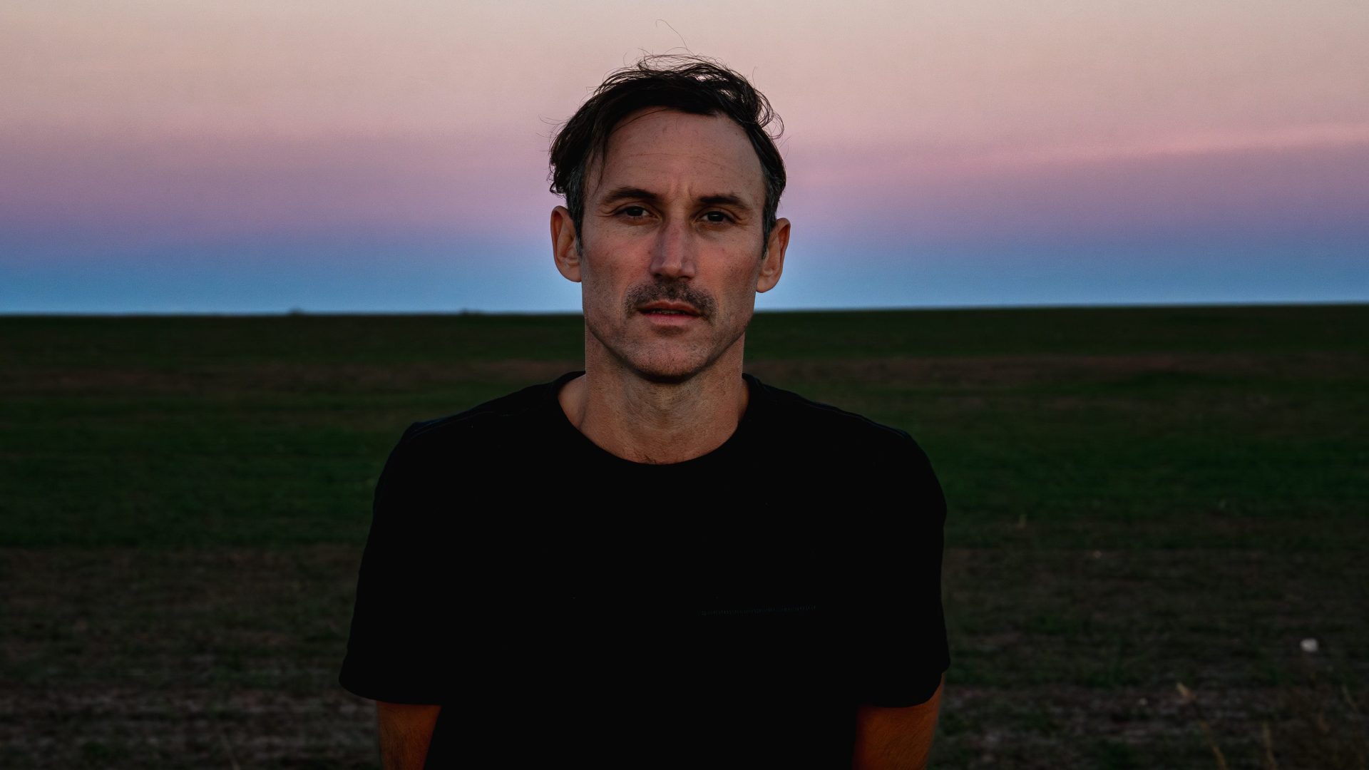 A man looks into the camera against a sunset backdrop.