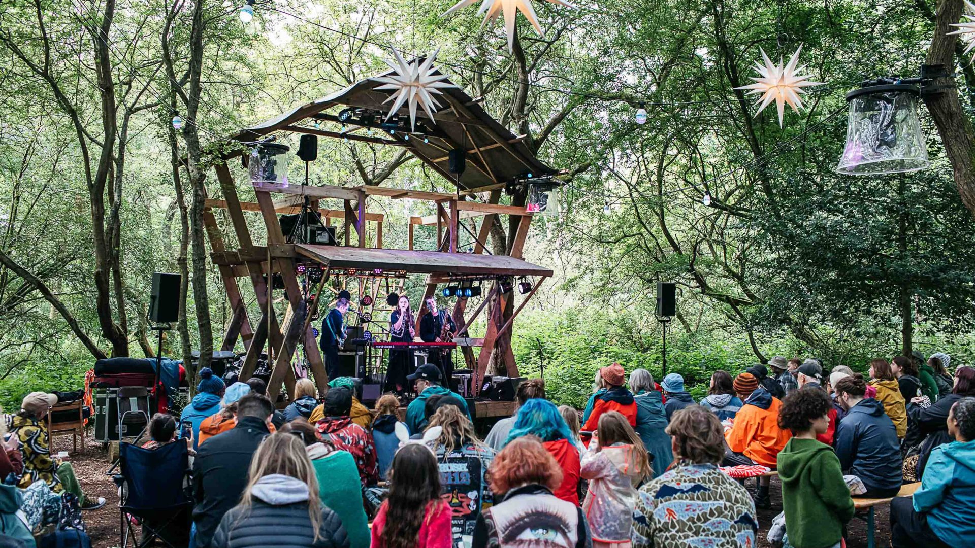 Festivalgoers watch live music performed from a wooden stage.