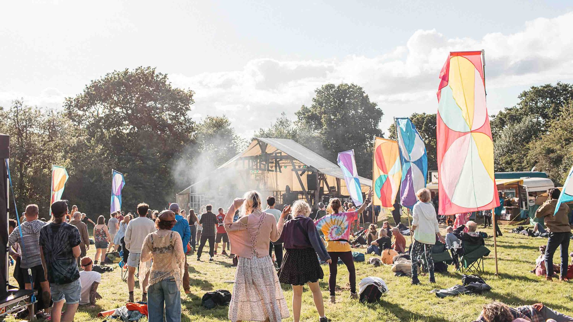 Festivalgoers dance on a lawn surrounded by colorful flags.