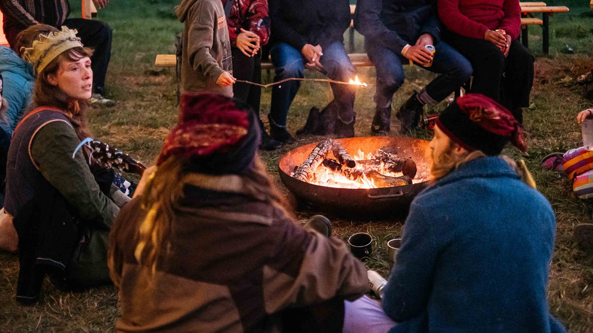 Festivalgoers sit around a campfire at night.